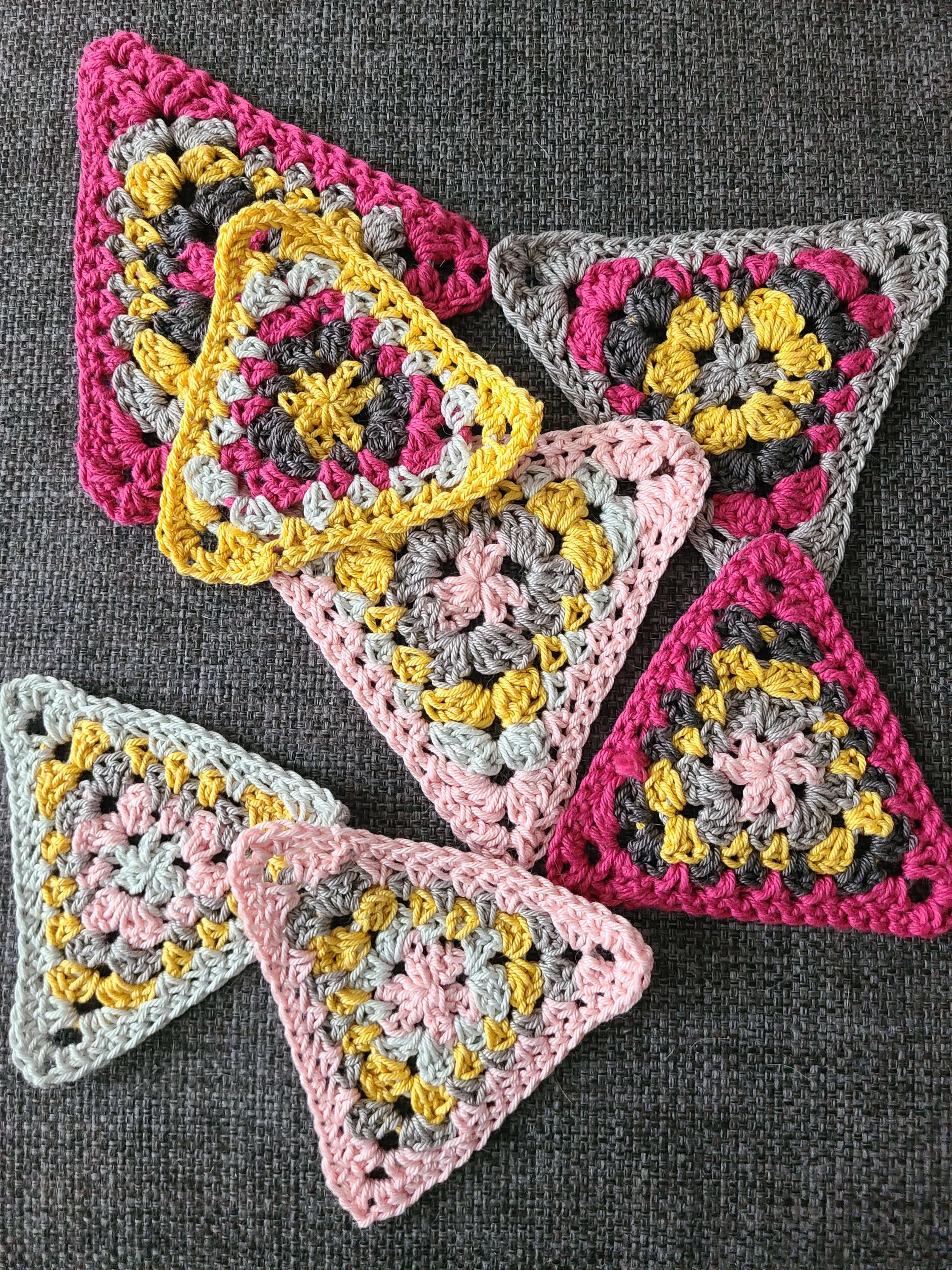 Photo of several crochet triangles in shades of yellow, pink, and gray.