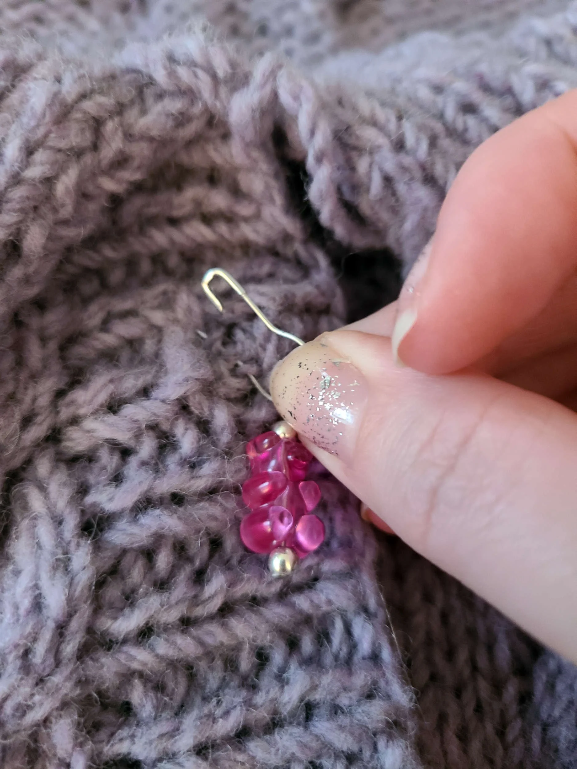 photo of an open stitch marker going through a button hole and picking up yarn on the next layer of fabric.