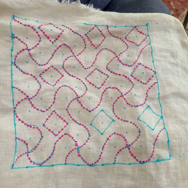Photo of a piece of linen fabric. A pattern has been drawn in blue marker, most of these lines have been stitched over with pink thread.