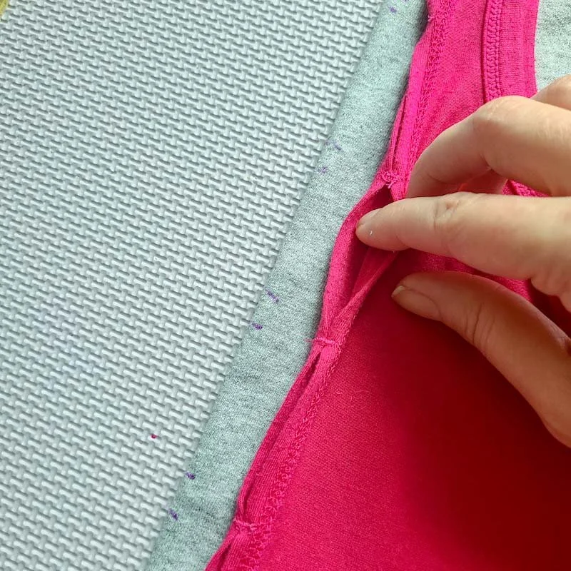Photo of a gray T-shirt folded in half lengthwise and laid flat. A pink Tank has been set on top. Purple marking on the T-shirt line up with the edges of holes in the pink tank.