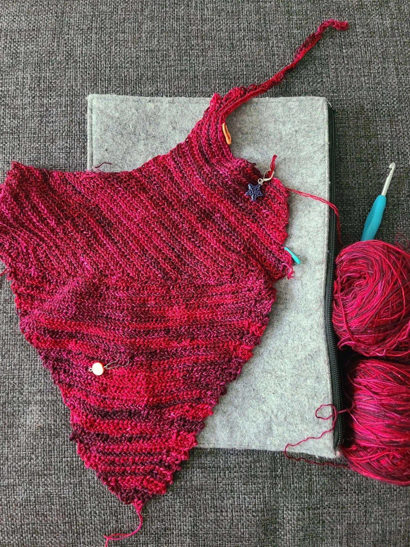 photo of an in progress crochet top made with two balls of red variegated yarn on a gray background.