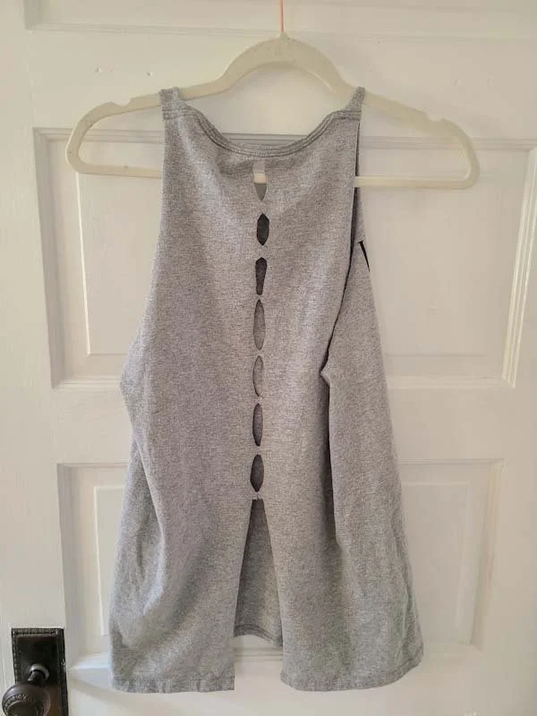 Photo of a gray tank on a hanger in front of a white door. The tank is seen from the back and has a T-back shape with a series of holes down the mid back.