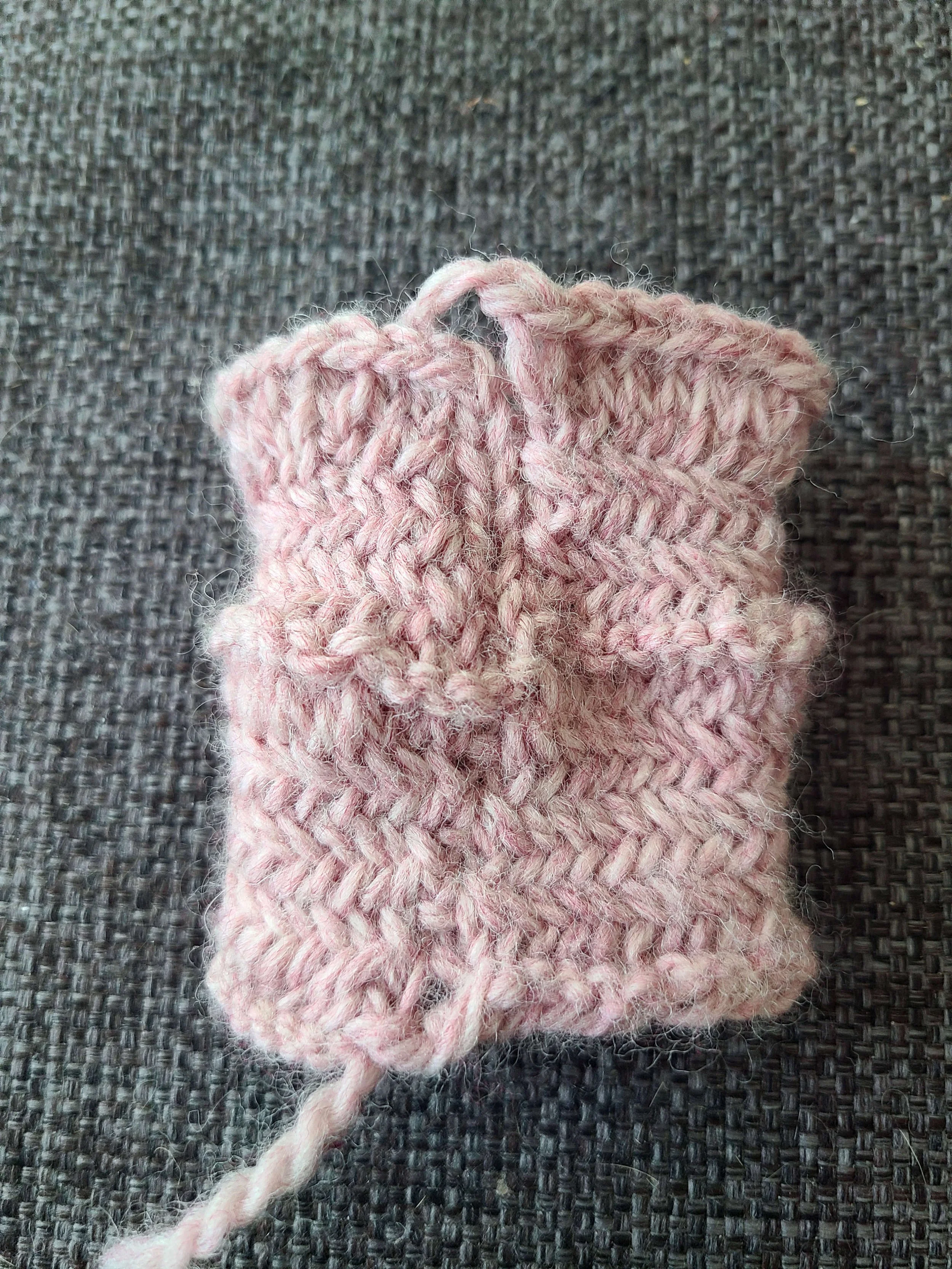 photo of an in the round swatch of herringbone stitch showing a very messy join on the lower half and the neater but more noticeable join when a knit stitch is added.