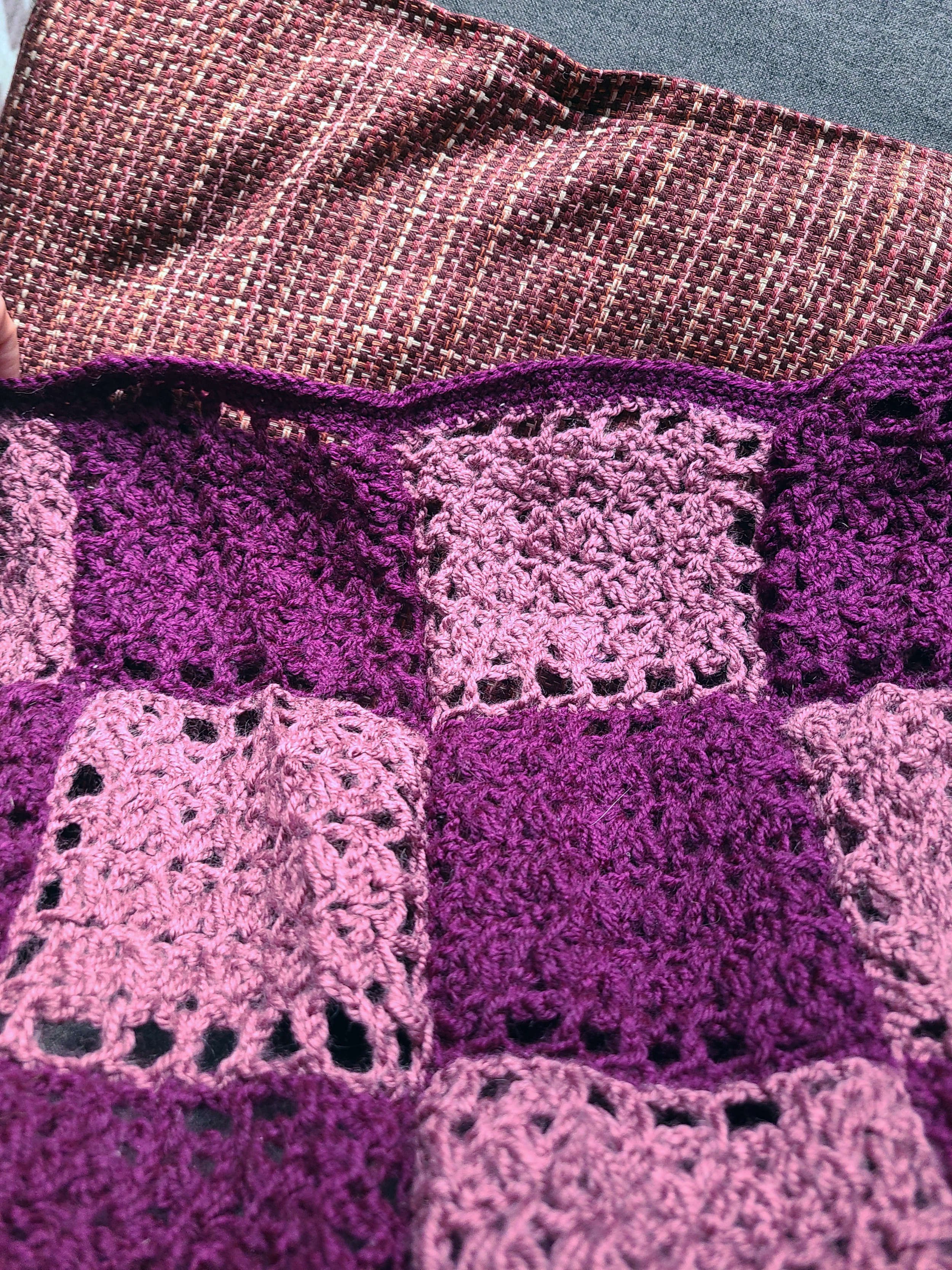 photo of the edging detail of a blanket consisting of light and dark purple crochet squares. The edging is dark purple, but bows slightly outward due to the squares being slightly uneven.