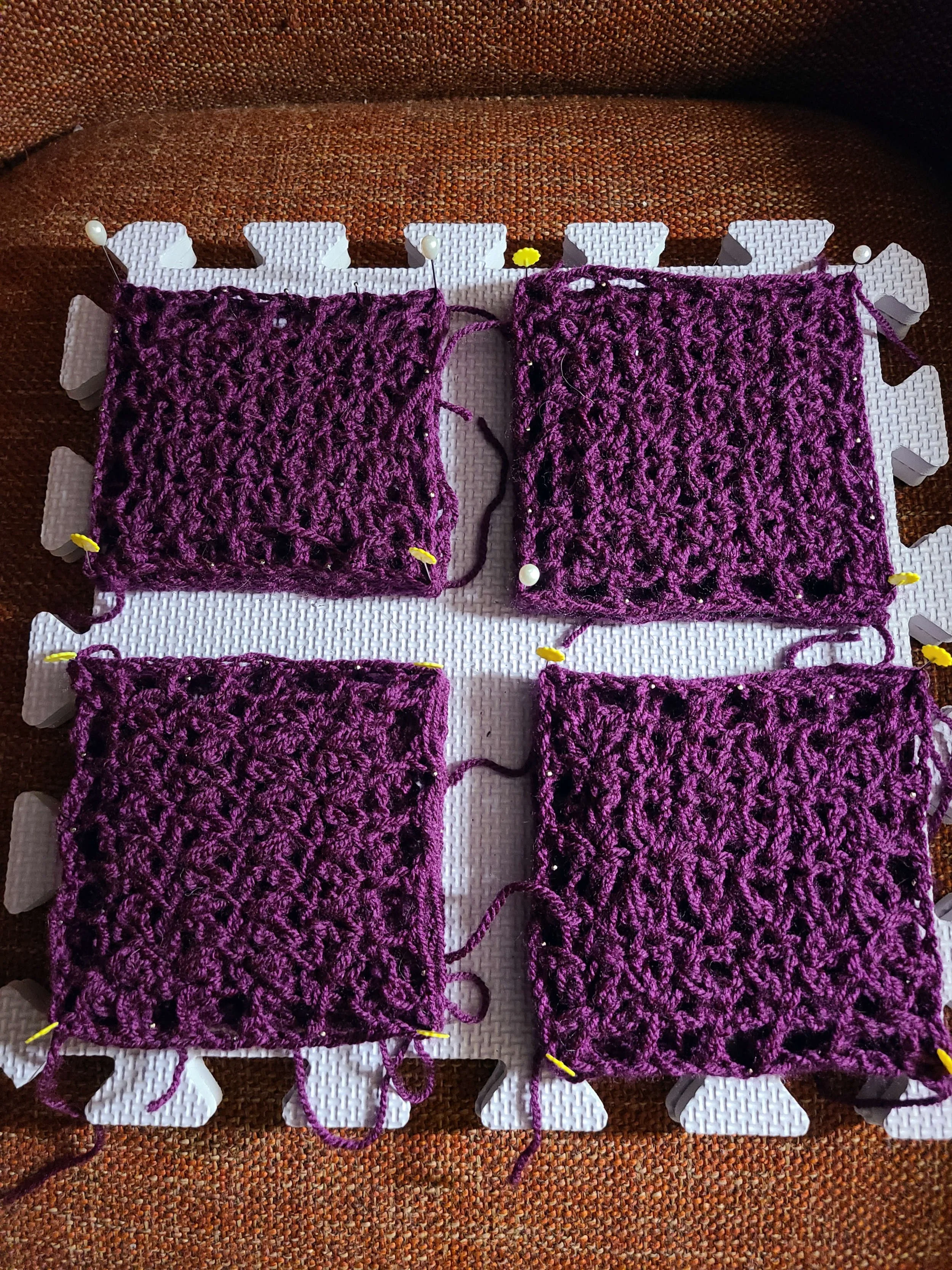photo of a foam blocking mat to which four crochet squares have been pinned.