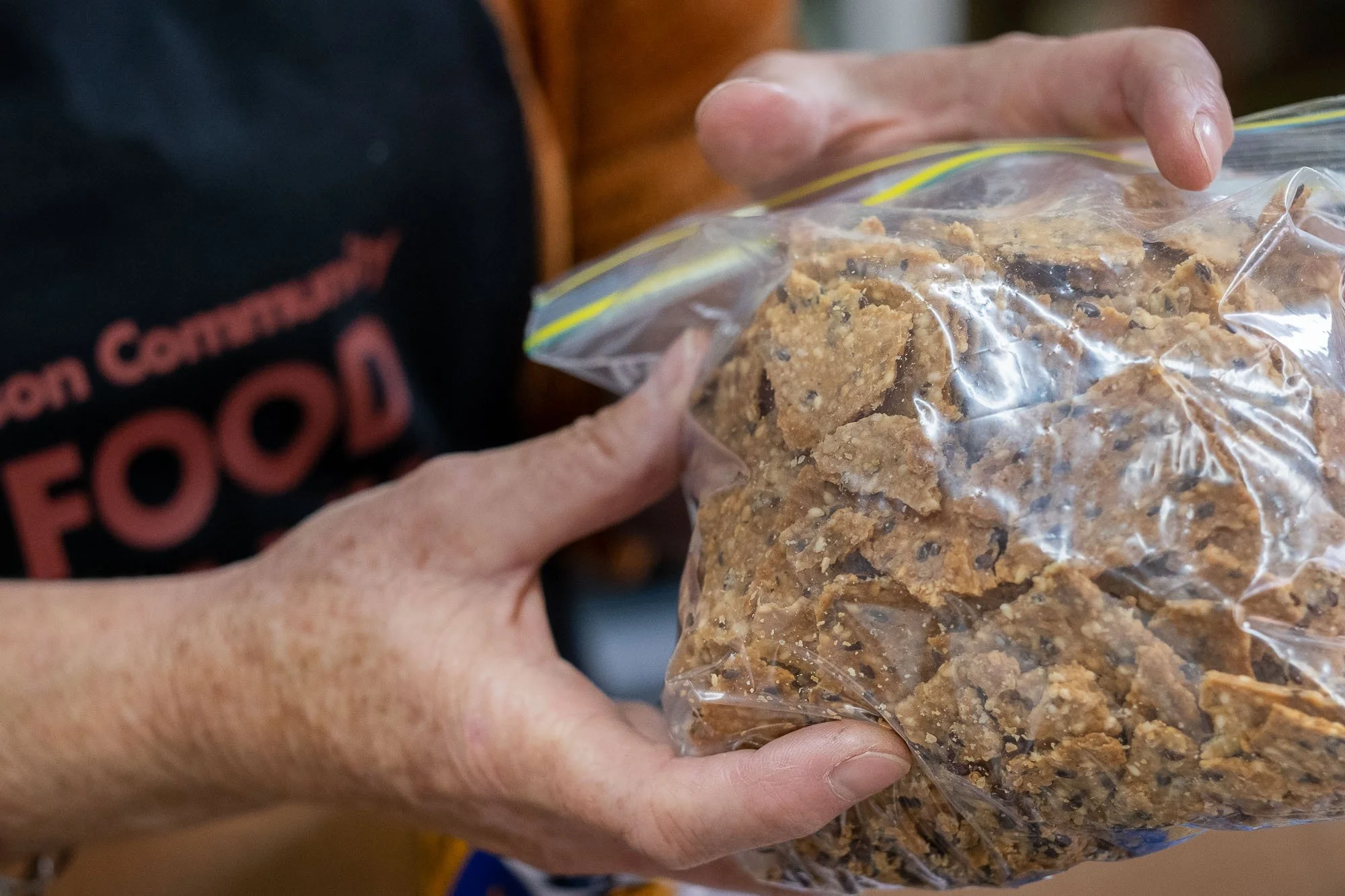 A person's hands holding a clear plastic bag filled with a crumbly, brown food mixture.
