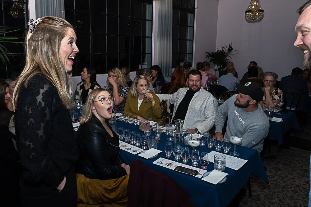 People participating in a tasting event, such as a whiskey or wine tasting, with glasses and tasting notes on the table.