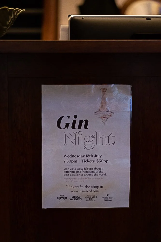 A poster advertising a 'Gin Night' event on Wednesday, July 13th at 7:30 pm with tickets priced at $50 each. The event will feature tasting and learning about four different gins from around the world, with information available at www.mamacod.com. T