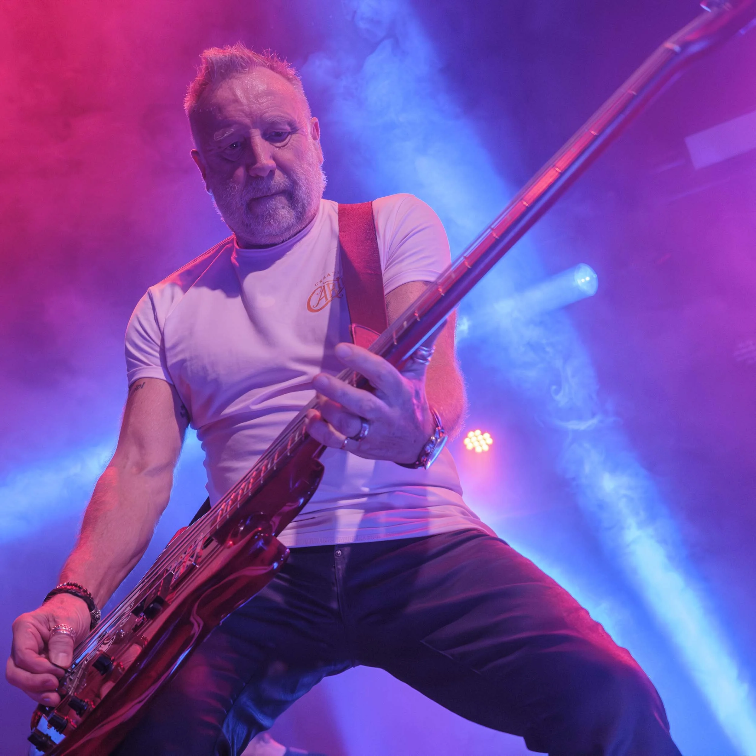 A man playing an electric guitar on stage, surrounded by colorful blue and pink lights and smoke.