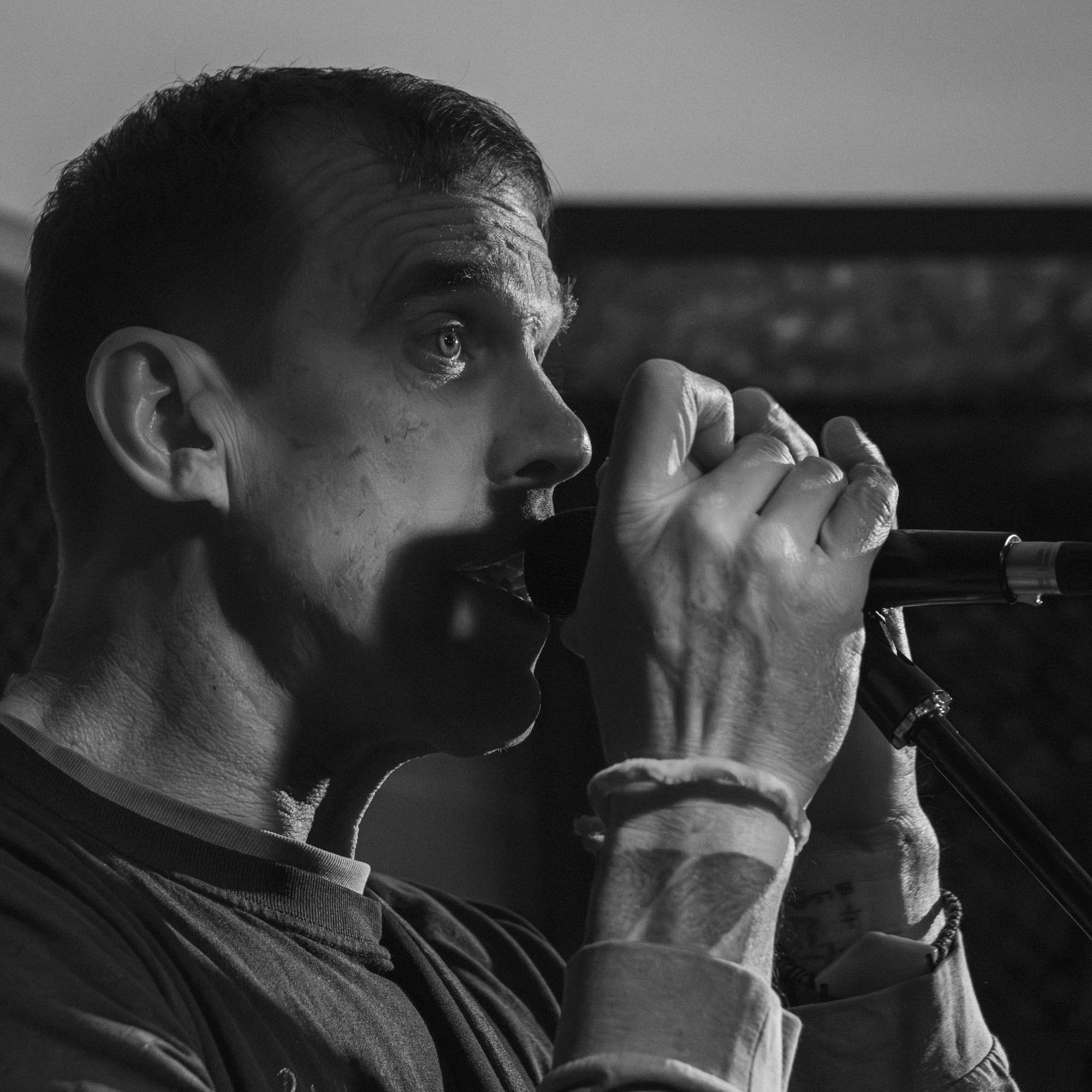 Black and white photo of a man with short hair and light-colored eyes, holding a vape or electronic cigarette near his lips.