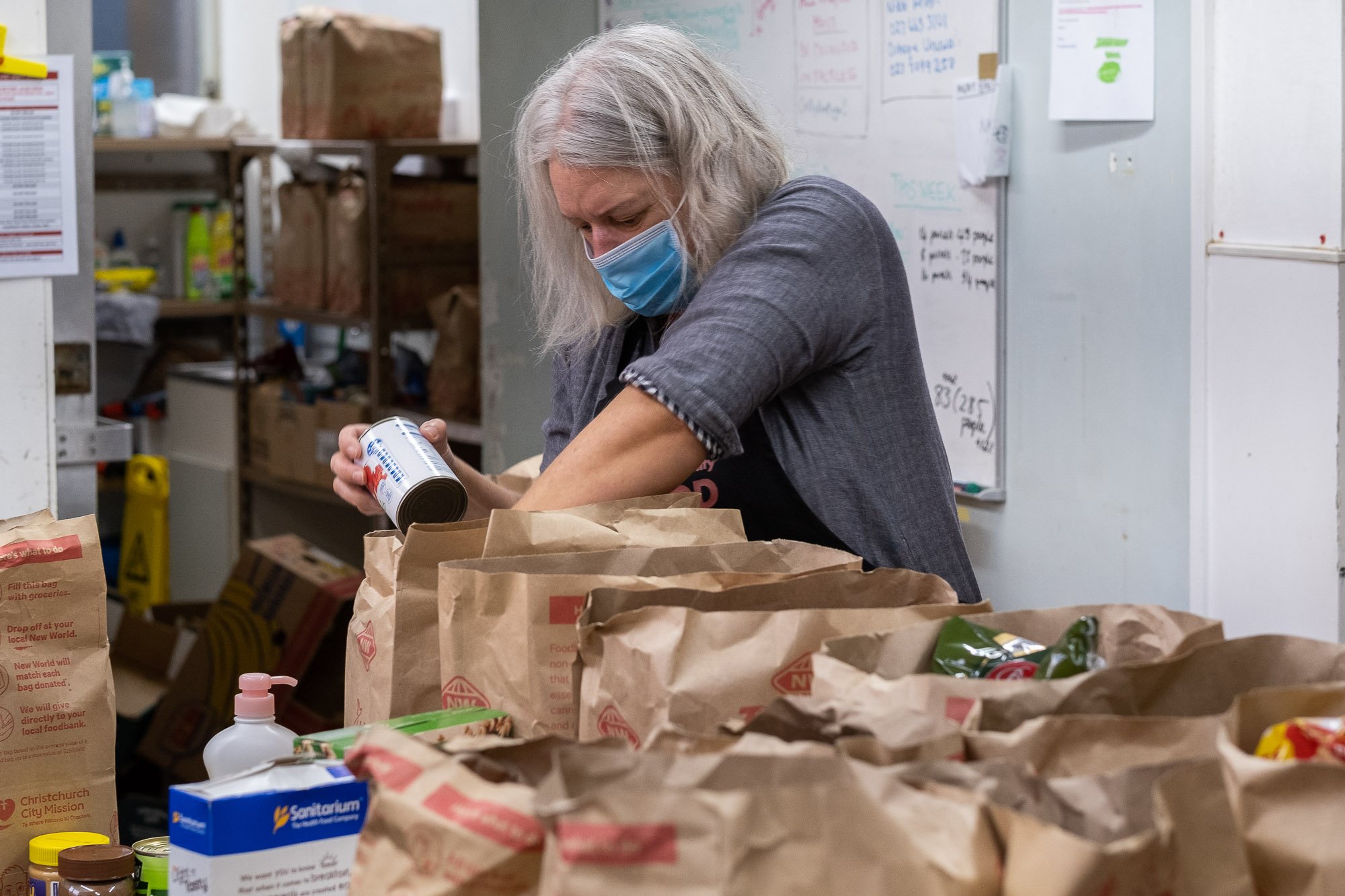 A woman wearing a face mask packing groceries into paper bags.