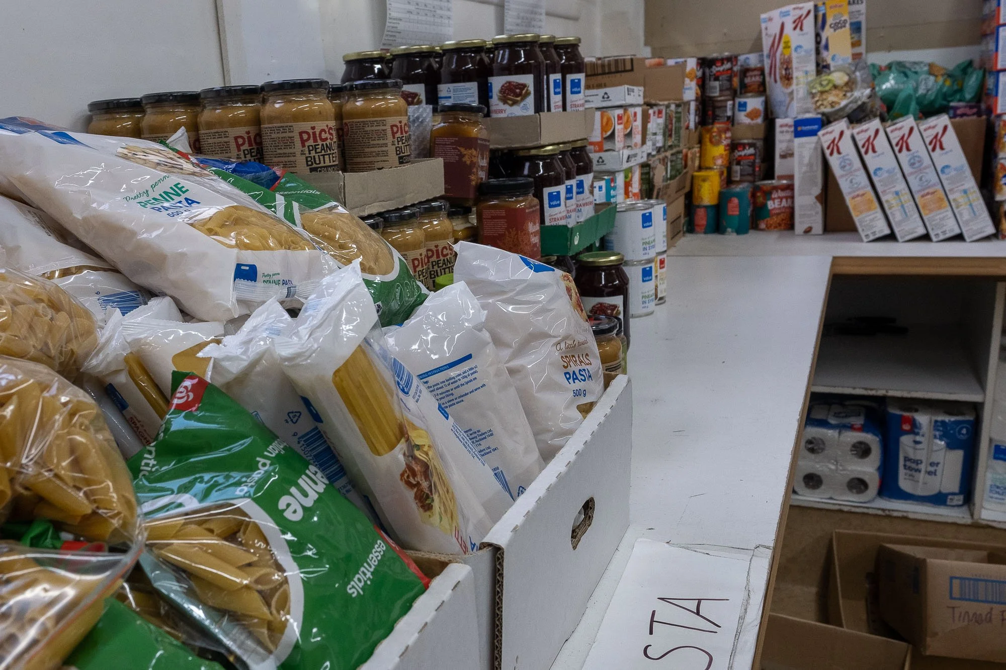 Store shelf with pasta, peanut butter, and canned goods.