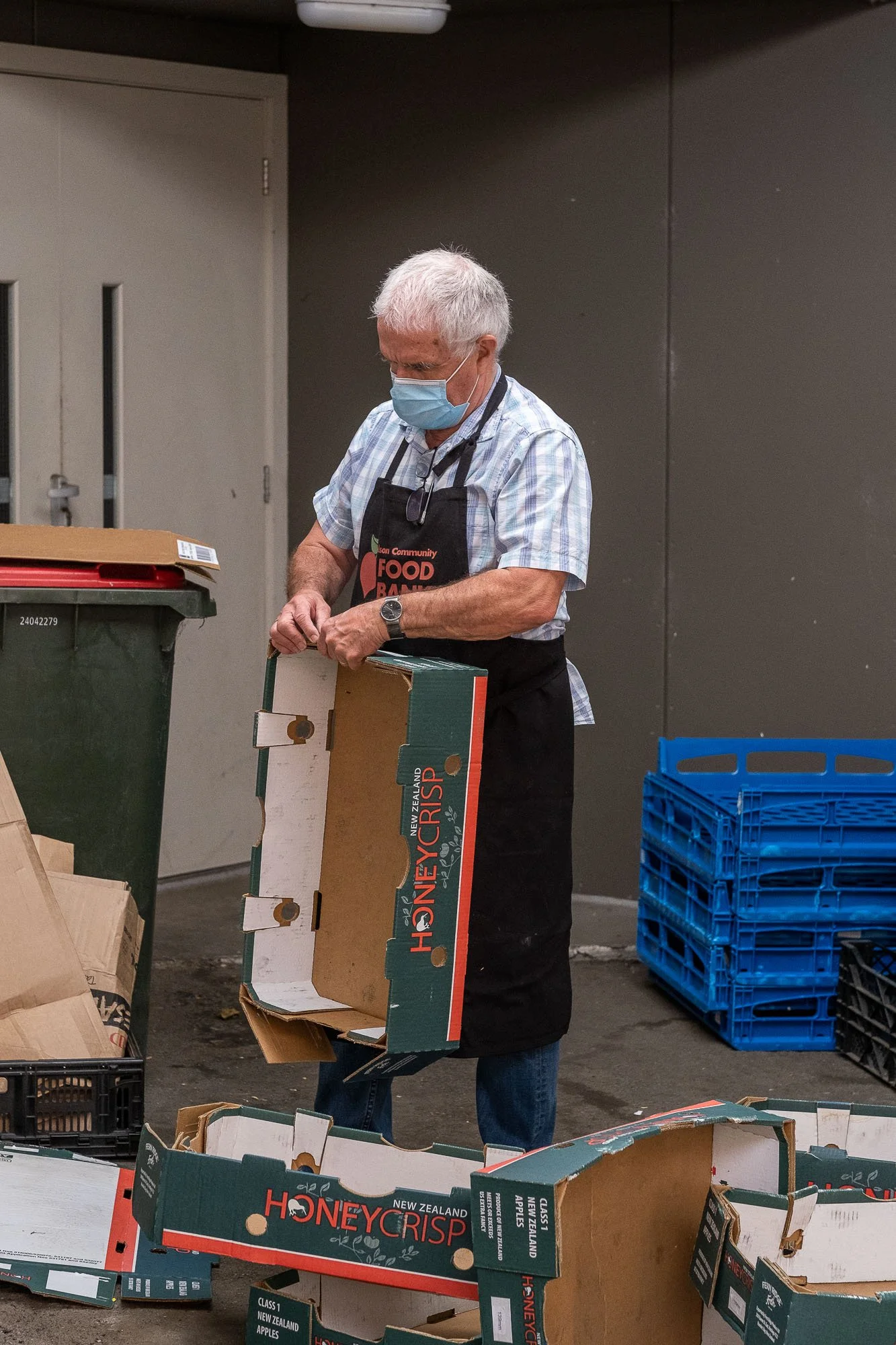 A man wearing a face mask and an apron is packing honeycrisp apple boxes in a storage or distribution area.