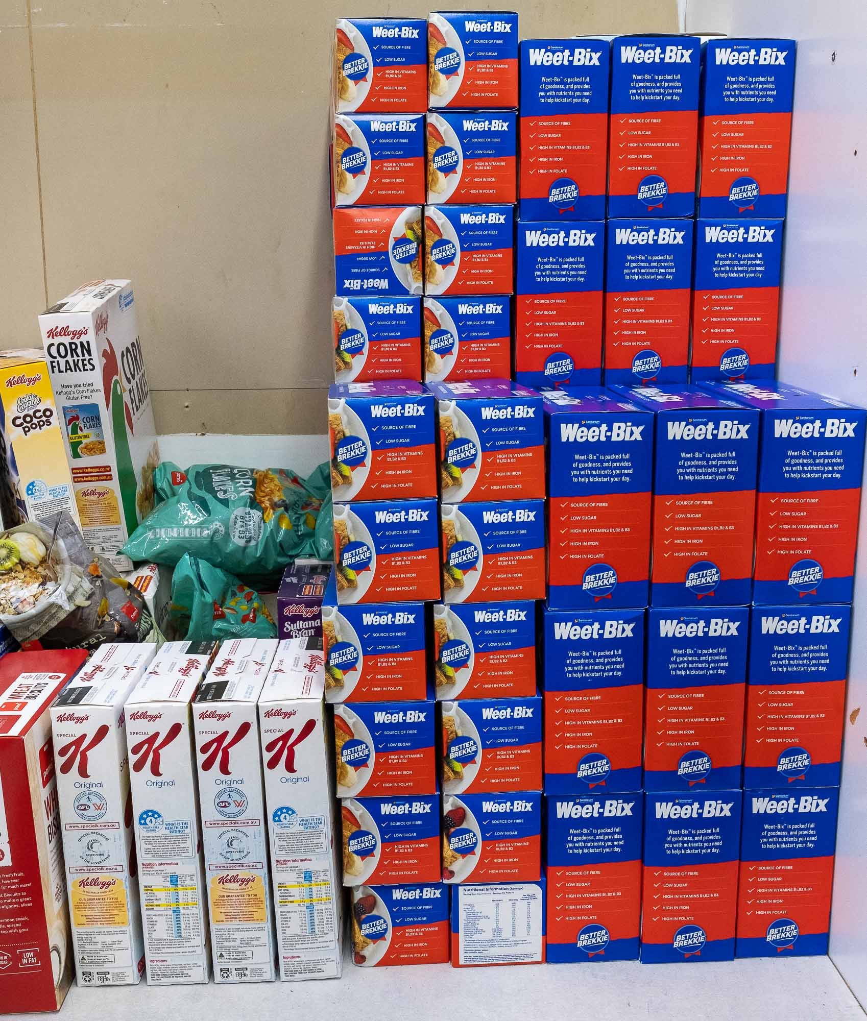 Display of multiple boxes of Weet-Bix cereal stacked on a table, with Kellogg's Corn Flakes cereals on the side.