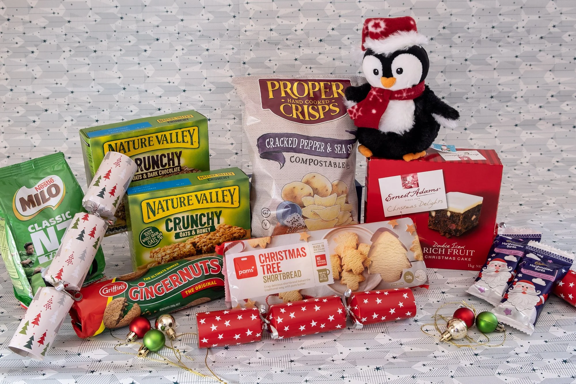 Assorted Christmas treats and decorations including snacks, a plush penguin wearing a Santa hat, and mini Christmas ornaments.