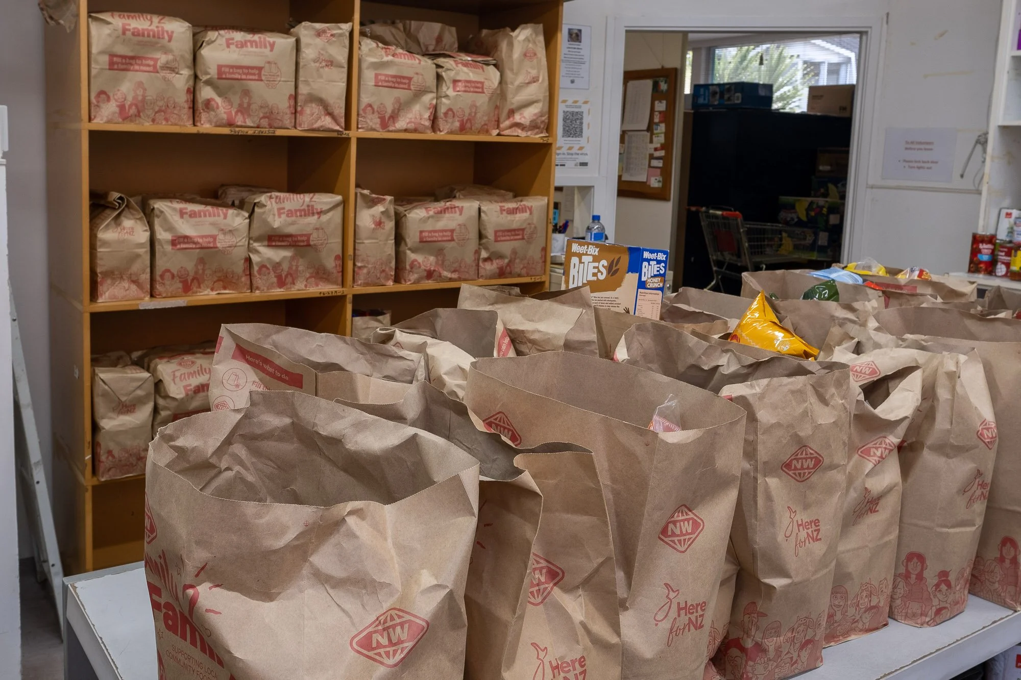 Brown paper grocery bags on a table with a store shelf filled with similar bags in the background.