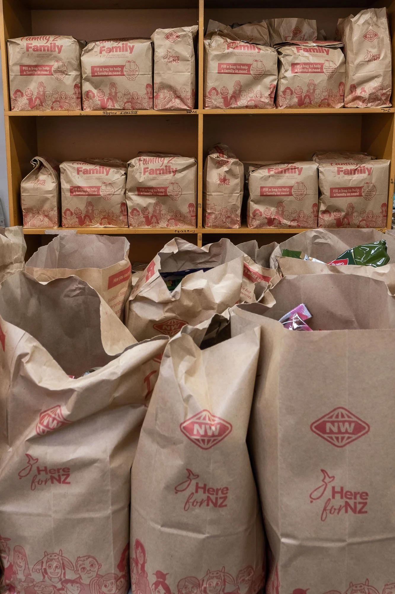 Shelf with brown paper bags labeled 'Here for NZ' and filled with donations.