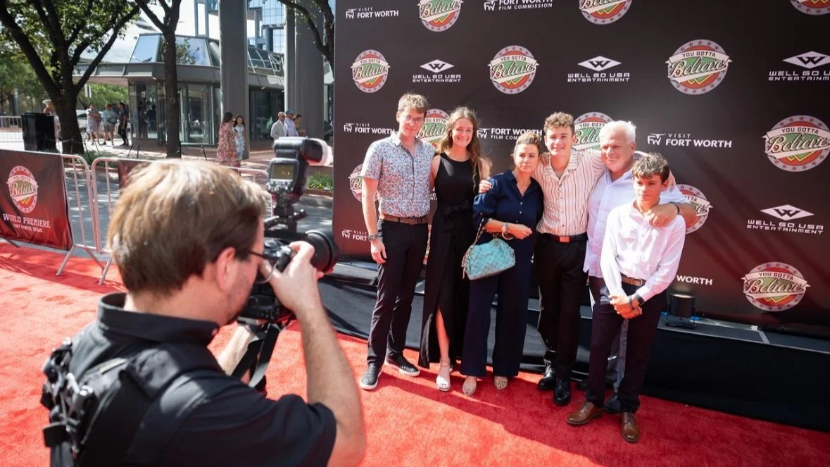 Cast poses in front of custom step and repeat at red carpet film premiere.