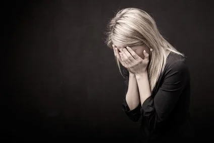 A woman with blonde hair covering her face with her hands, appearing upset or distressed