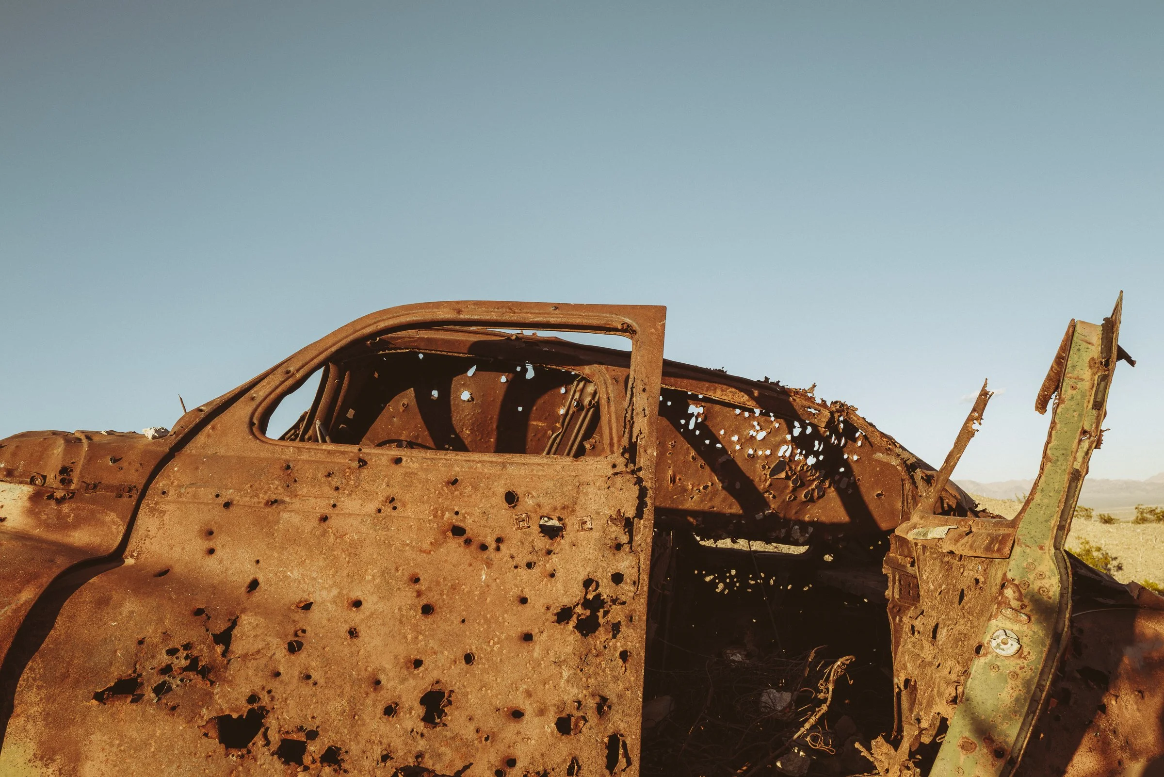 Rusty, abandoned car in a desert landscape under a clear blue sky.