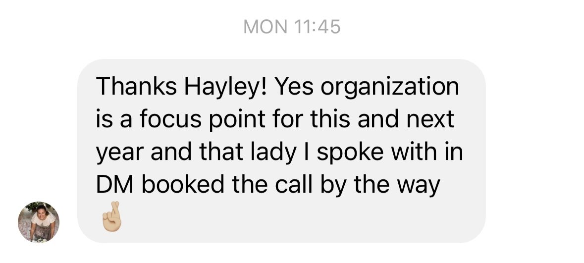Text message on a mobile phone screen reading: "Thanks Hayley! Yes organization is a focus point for this and next year and that lady I spoke with in DM booked the call by the way" with a small profile picture of a woman in a white shirt and a finger-crossing emoji.