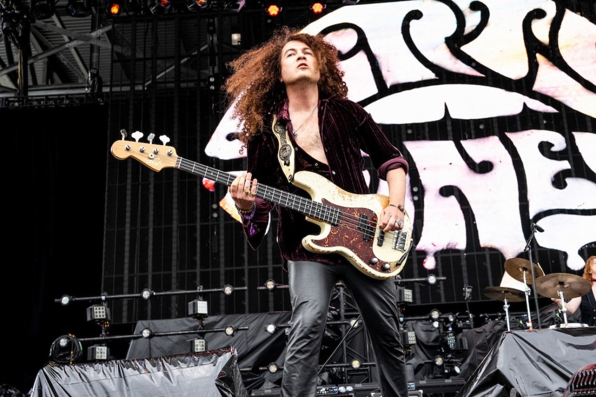 Musician with curly hair playing electric bass guitar on stage during a live performance.