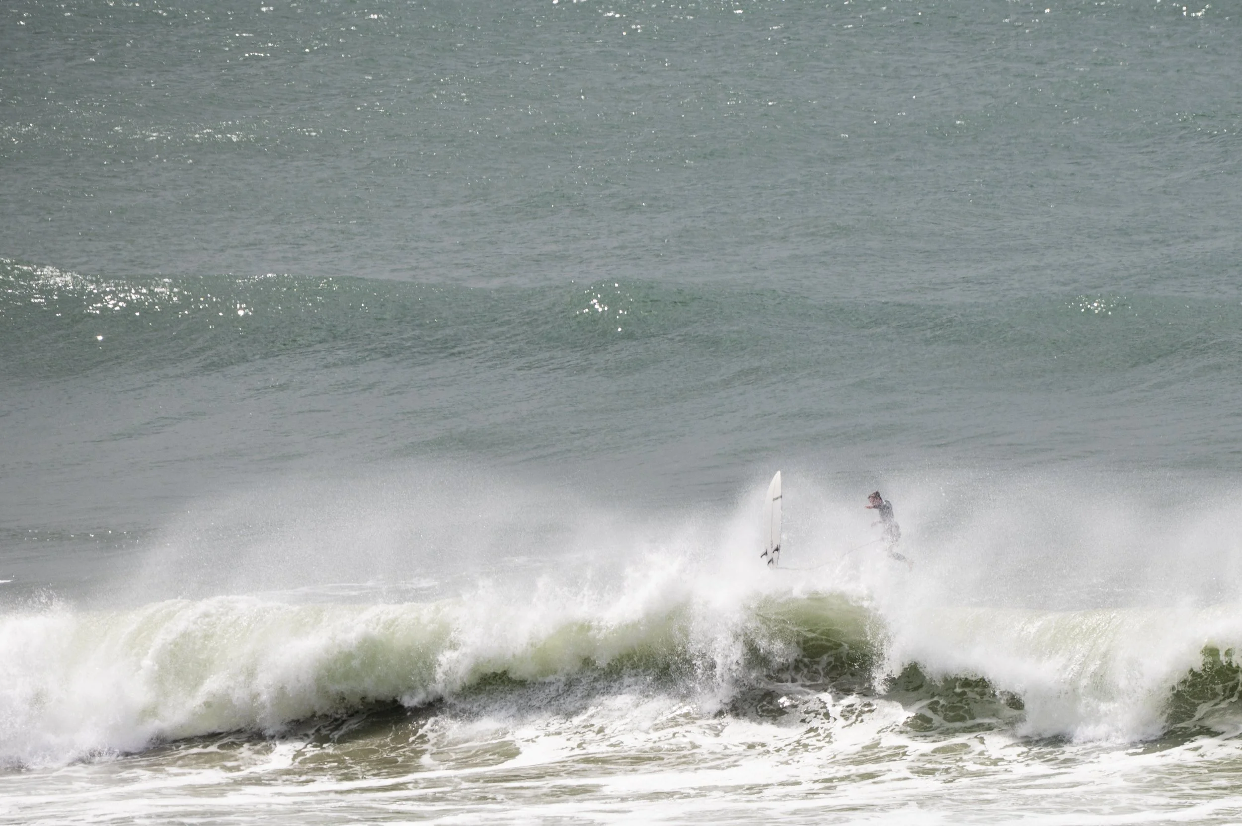 Person surfing on a wave at the beach with a surfboard.