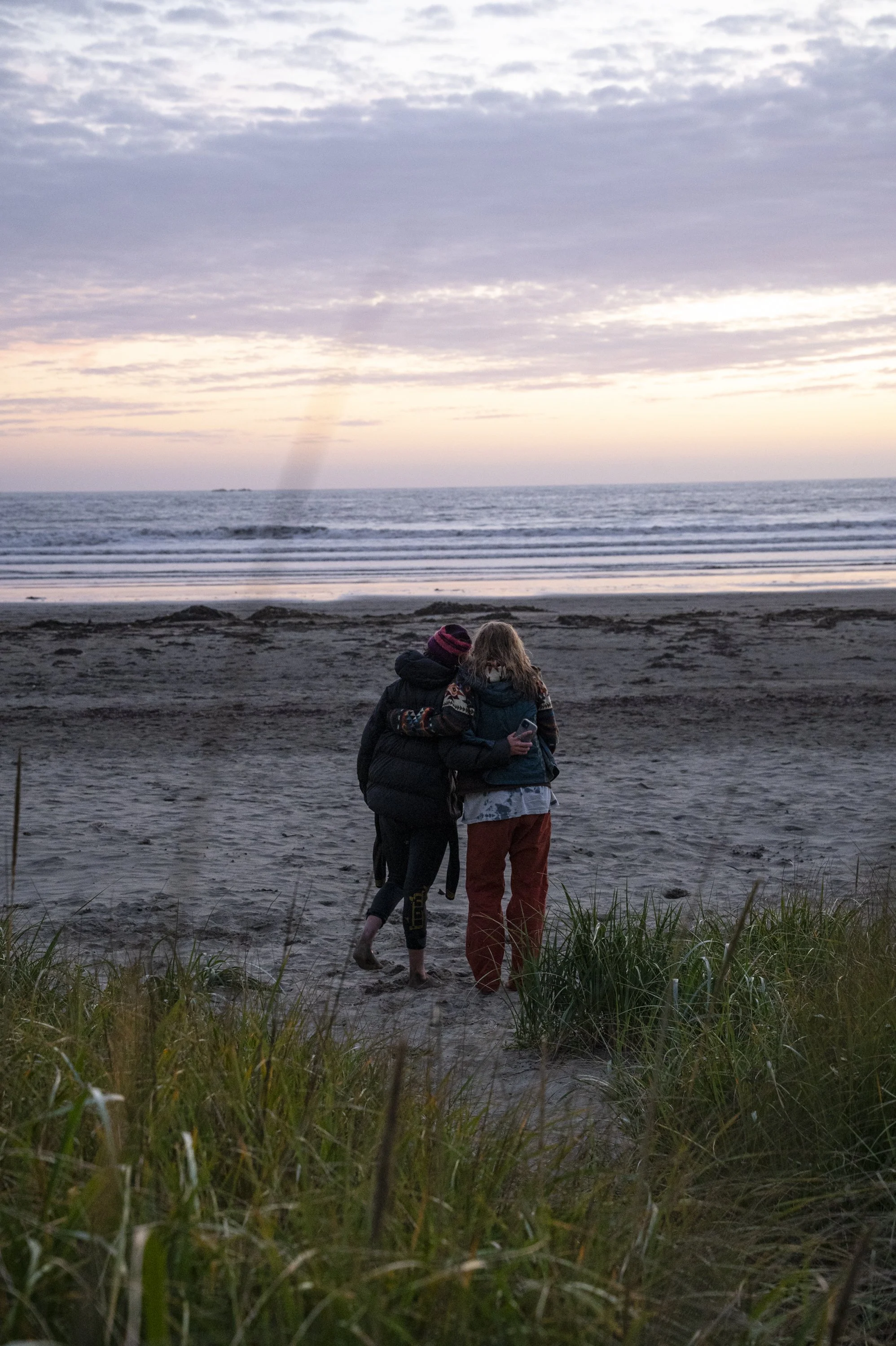 Two children walking along the beach at sunset, embracing and looking at the ocean.