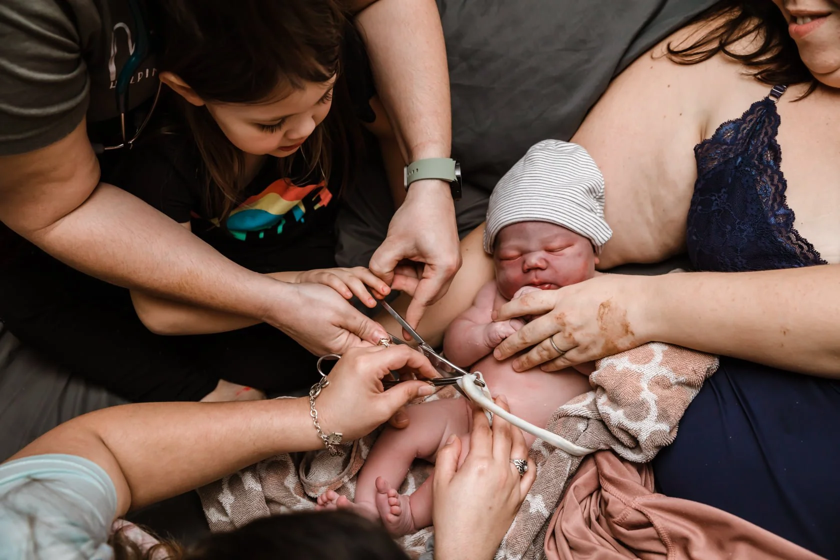 Big sister helping cut her new sibling's umbilical cord with the midwife's guidance after a home birth