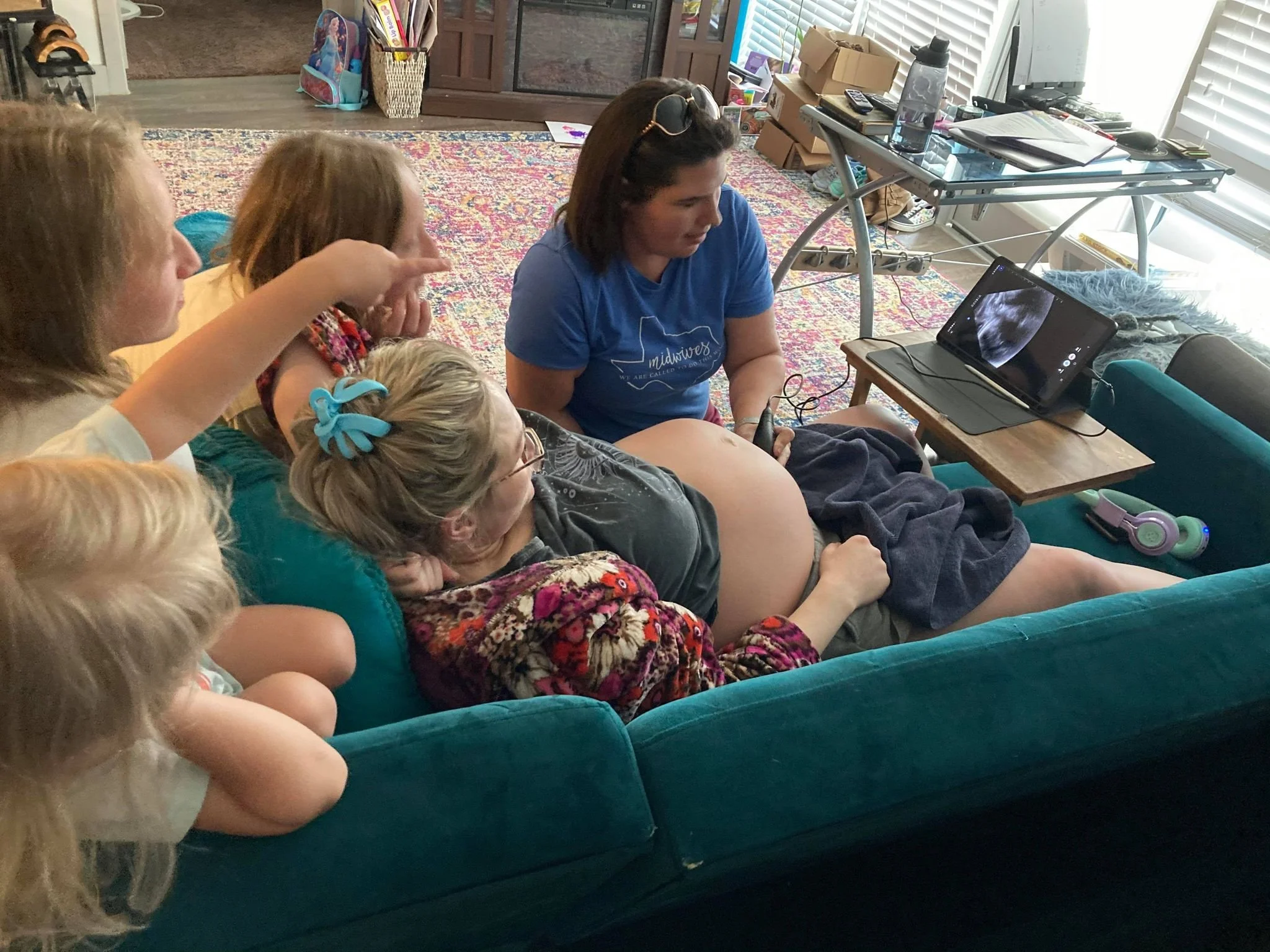 Midwife Amy performing an in-home prenatal ultrasound while the mother and her children watch the screen