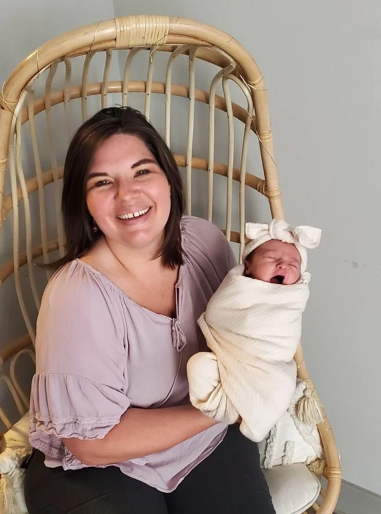Midwife Amy smiling while holding a swaddled, yawning newborn during a postpartum visit