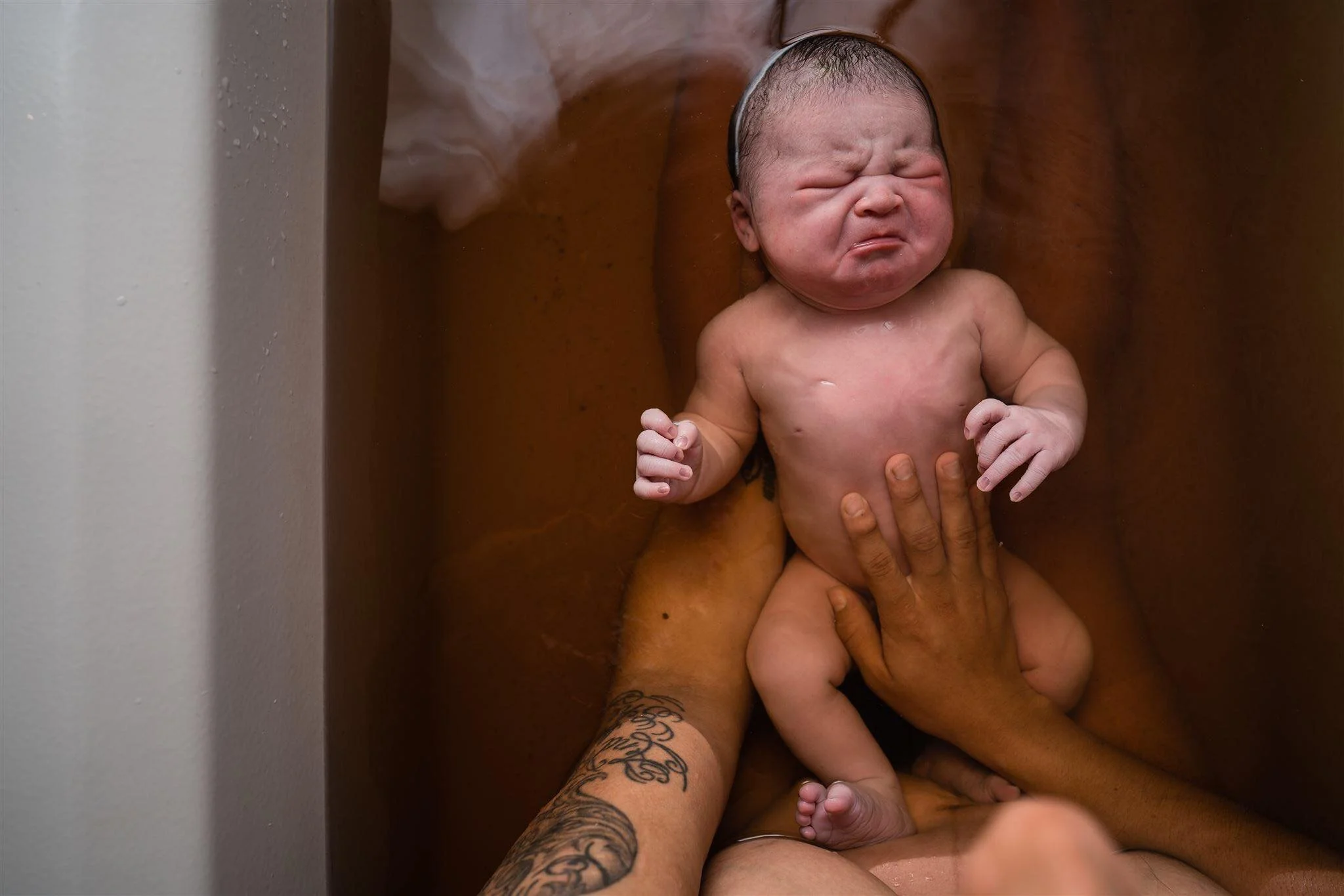Newborn baby held in her parents' hands moments after being born in the water at home