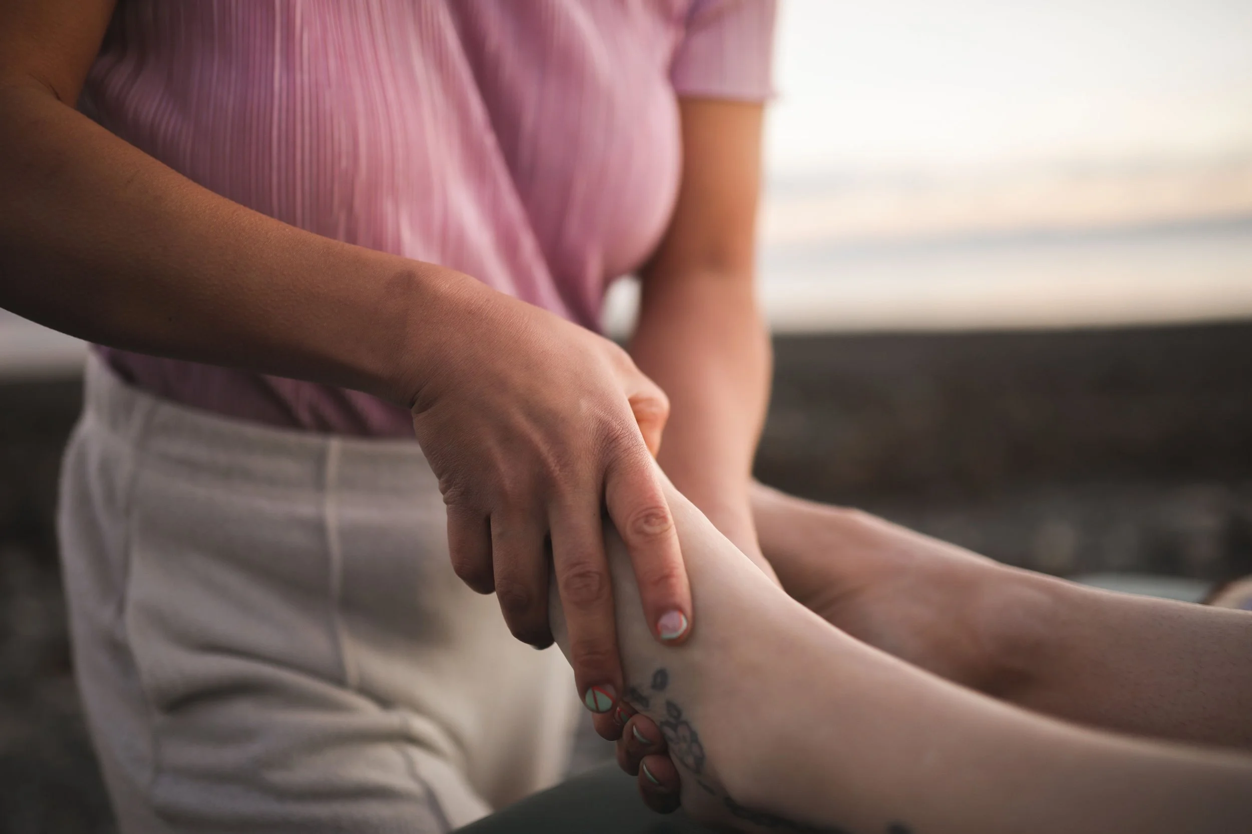 Person wearing a pink striped shirt touching the leg of another person with tattooed tattoos and a decorative nail art design.