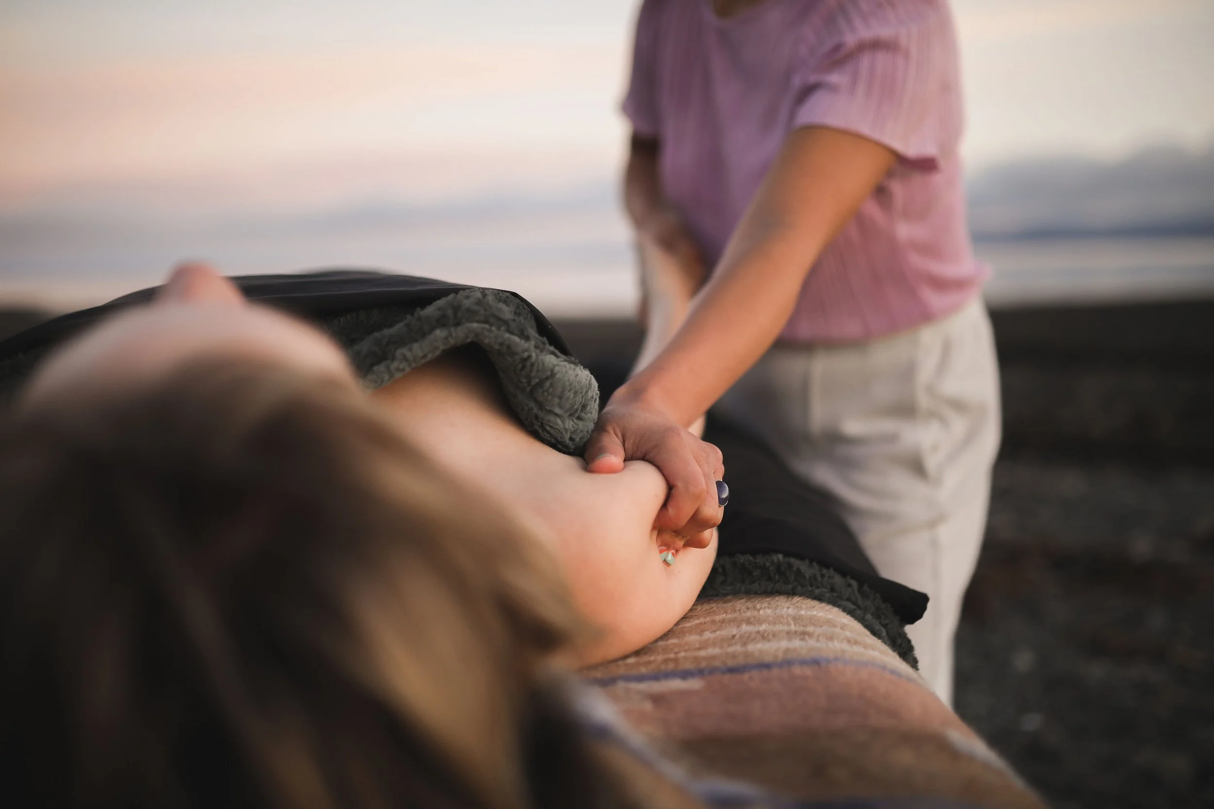A person receiving a massage outdoors during sunset on the beach.