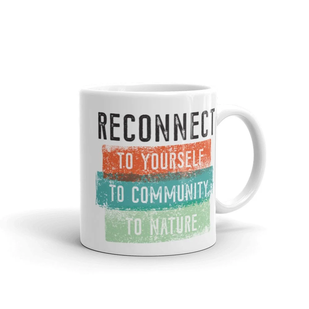 Merch design, mantra A white ceramic mug with colorful text that reads "Reconnect to yourself, to community, to nature."