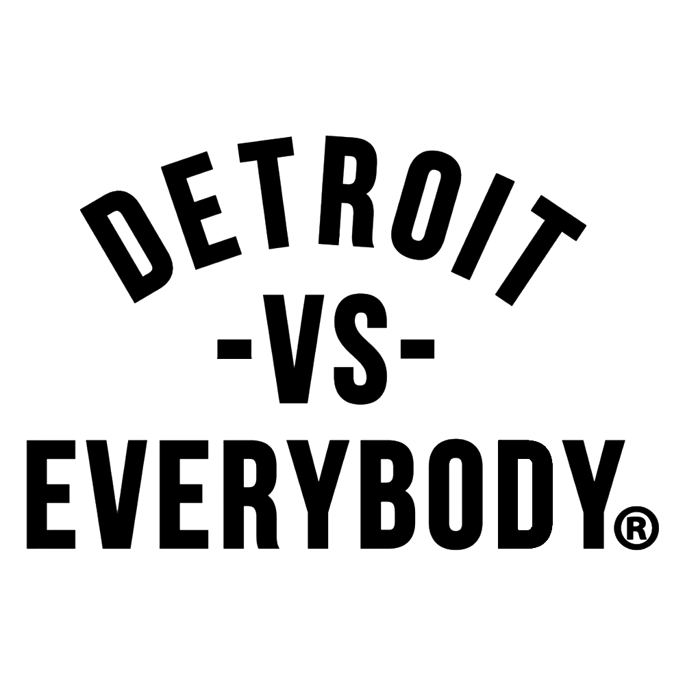 Black and white logo with the text 'Detroit vs Everybody' arranged in a curved manner, with 'Detroit' at the top, 'vs' in the middle, and 'Everybody' at the bottom.