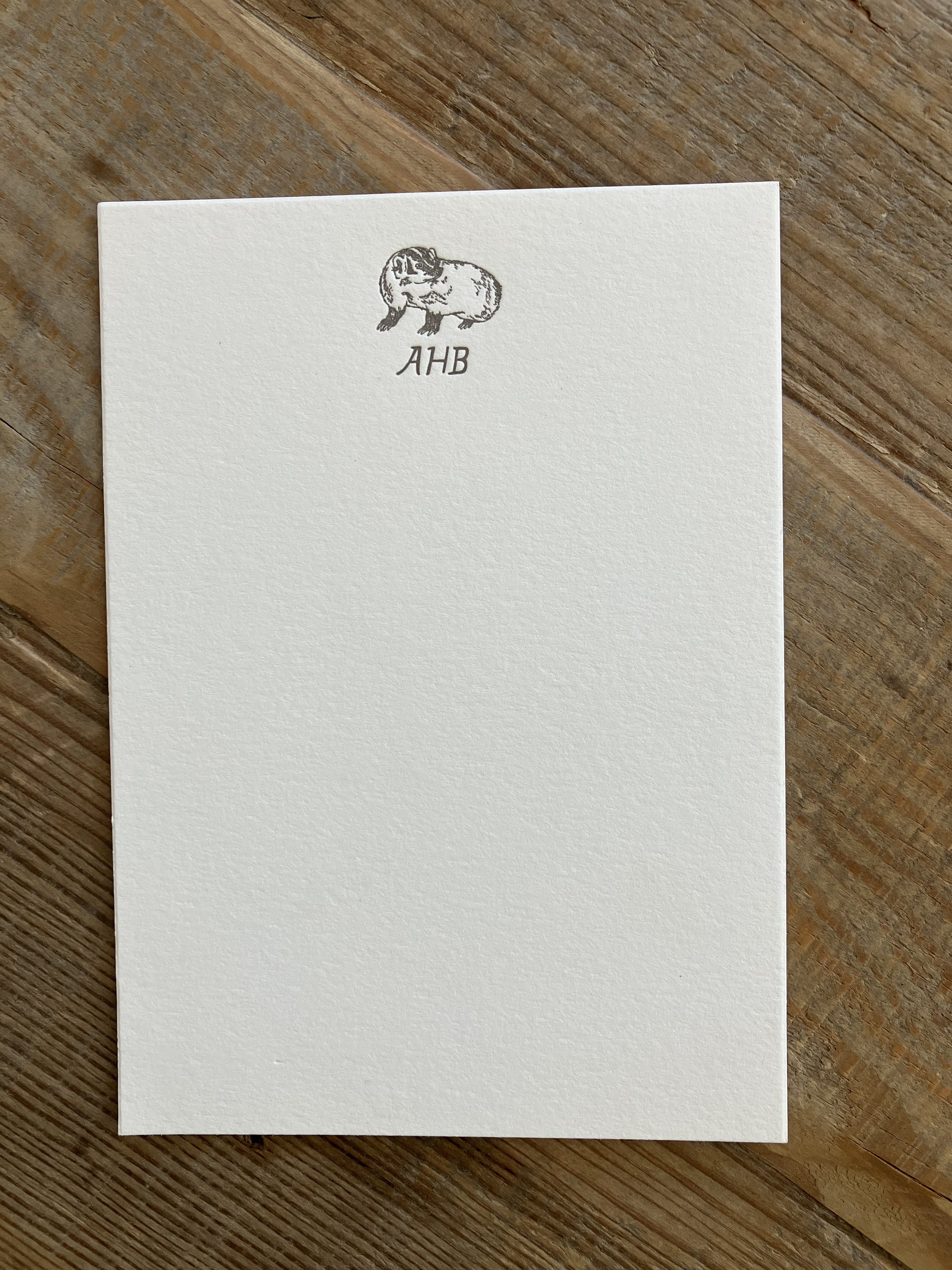 Blank paper with "AHB" and a sketch of an animal at the top, placed on a wooden surface.