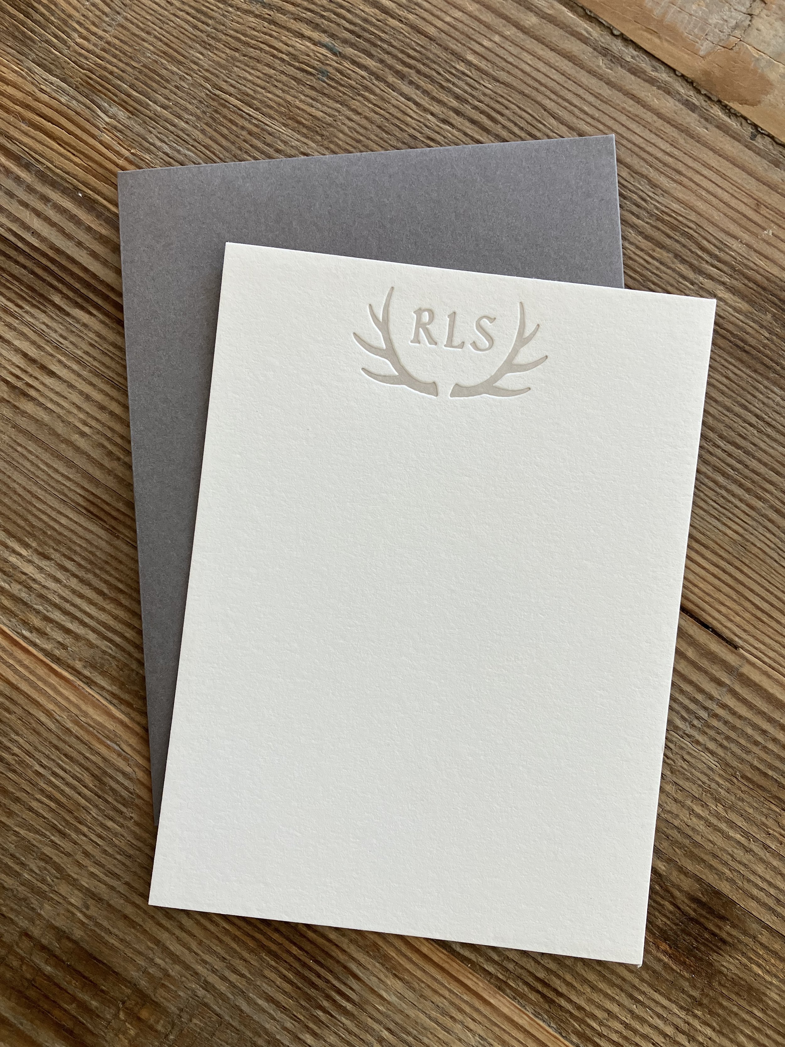 Embossed stationery with "RLS" initials and antler design on wooden surface.