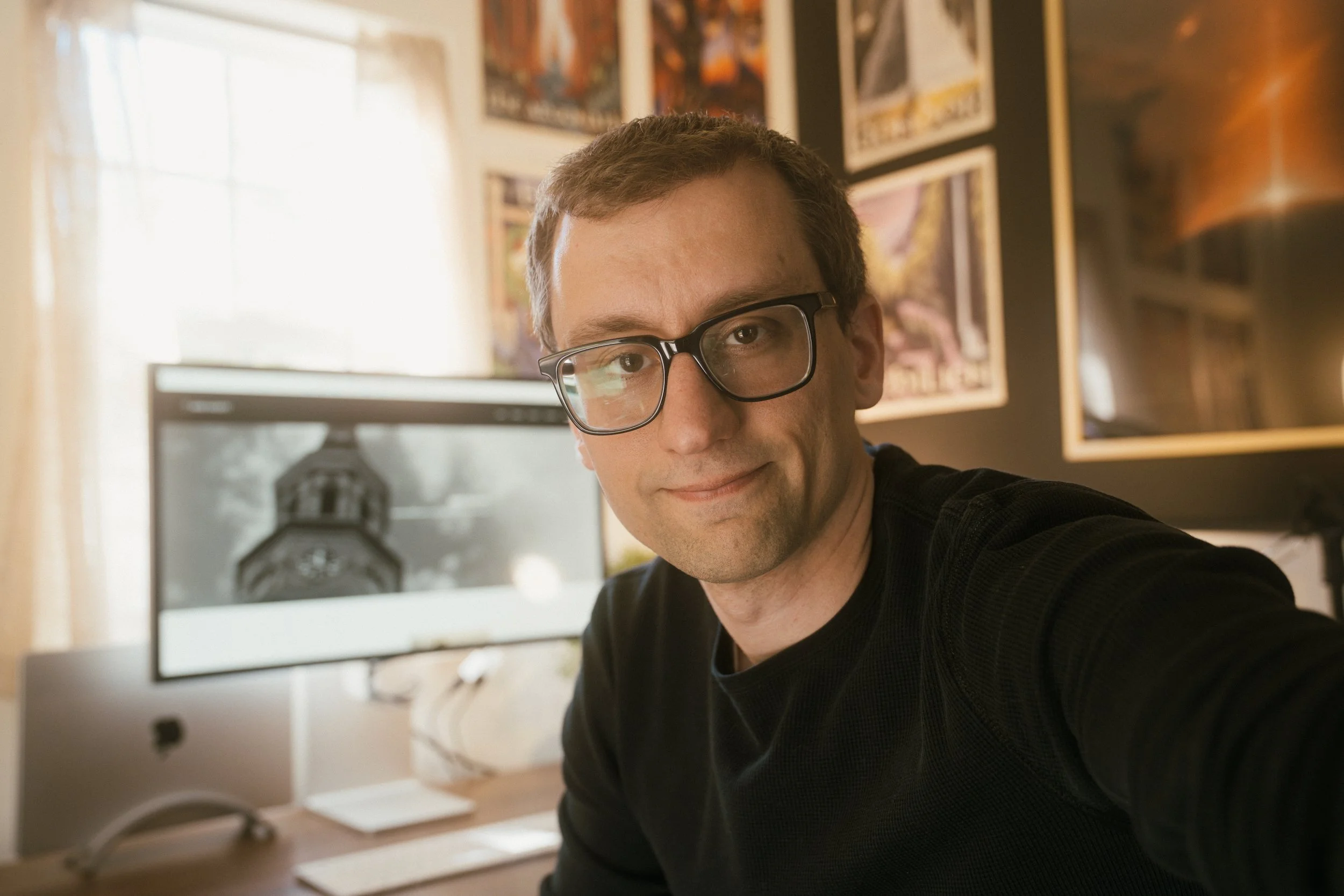 Photo of Mark Hackett in his office with a computer monitor and framed pictures on the wall behind him.