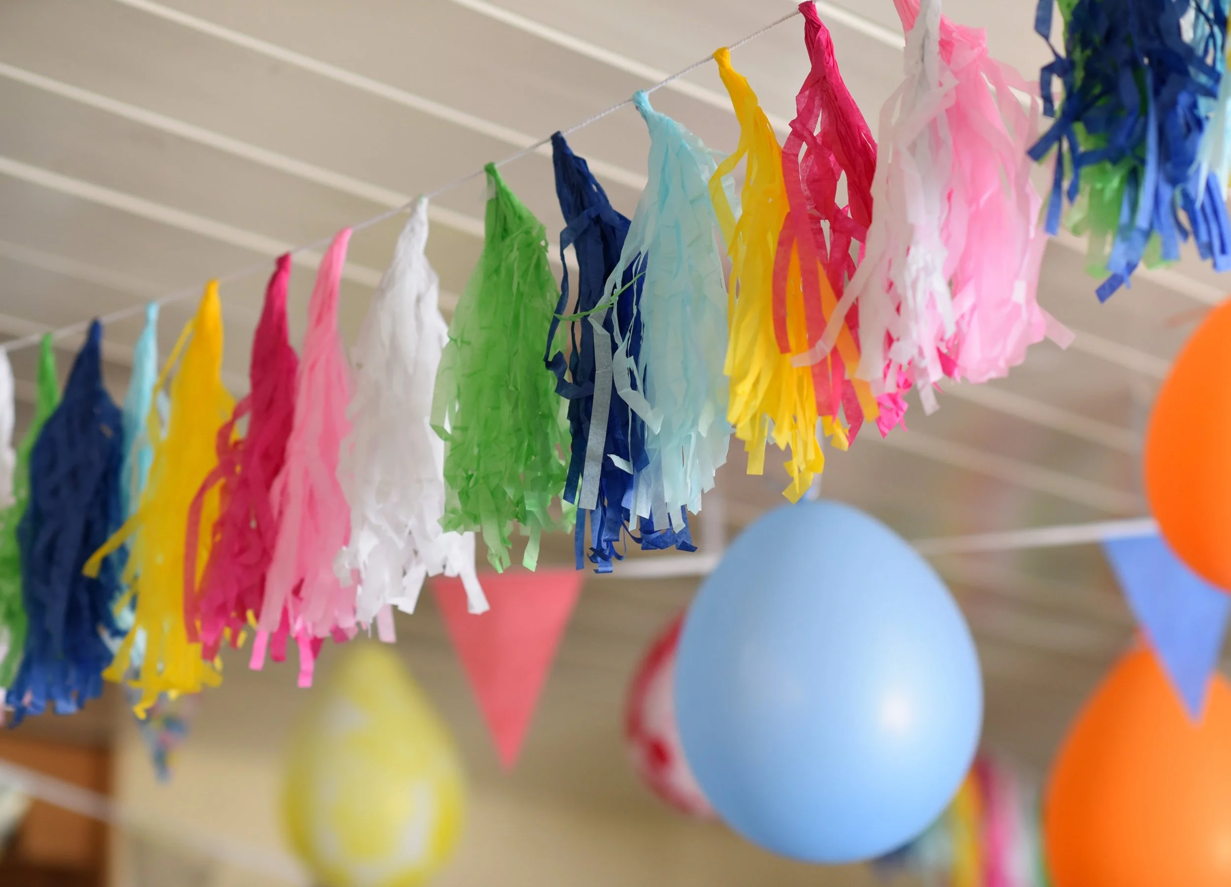 Colorful tissue paper garlands hanging from a string, with blue balloons in the background.