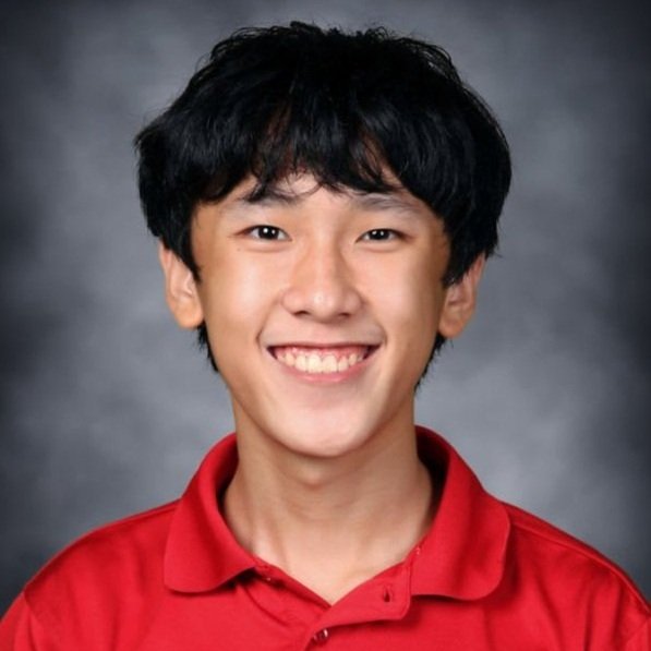 A young man with black hair smiling, wearing a red polo shirt against a gray background.