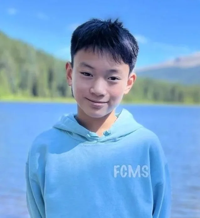 Confident young boy standing with arms crossed, wearing a bright yellow T-shirt with black text and designs, against a plain white background.