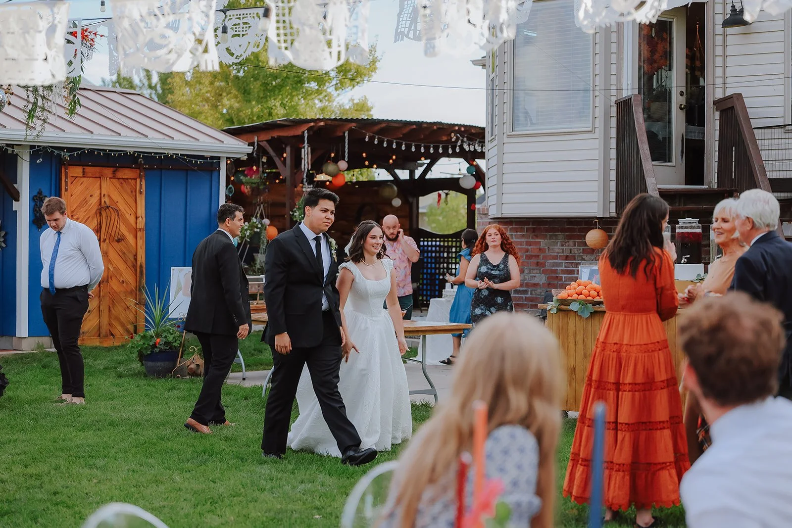Photograph of a bride and groom in front of colorful decor for their backyard wedding reception