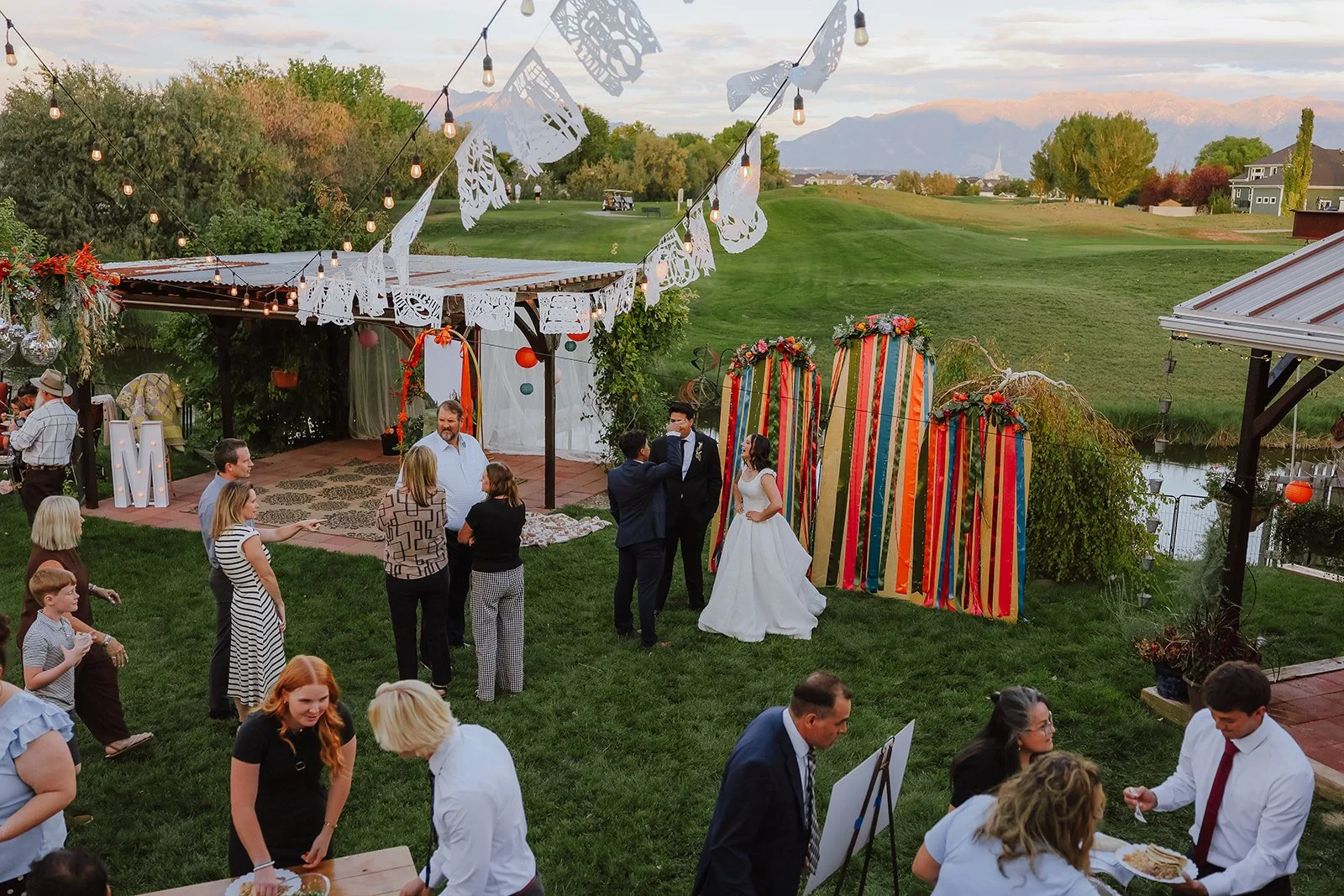 Photograph of a bride and groom in front of colorful decor for their backyard wedding reception syracuse, utah
