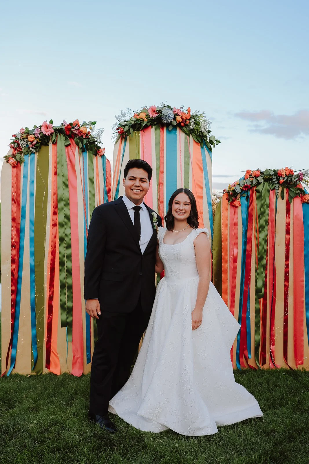 Photograph of a bride and groom in front of colorful decor for their backyard wedding reception