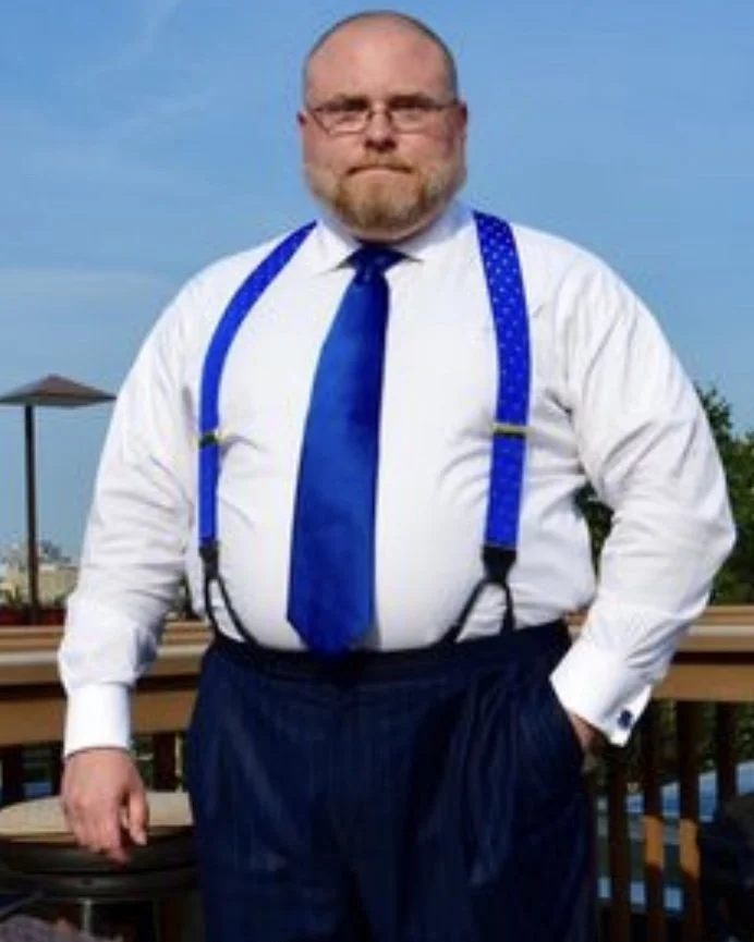 Frank, a large man, was recently voted one of the top defense attorneys in Los Angeles. He stands tall & overweight in a white button down blouse, blue suspenders, and matching work trousers.