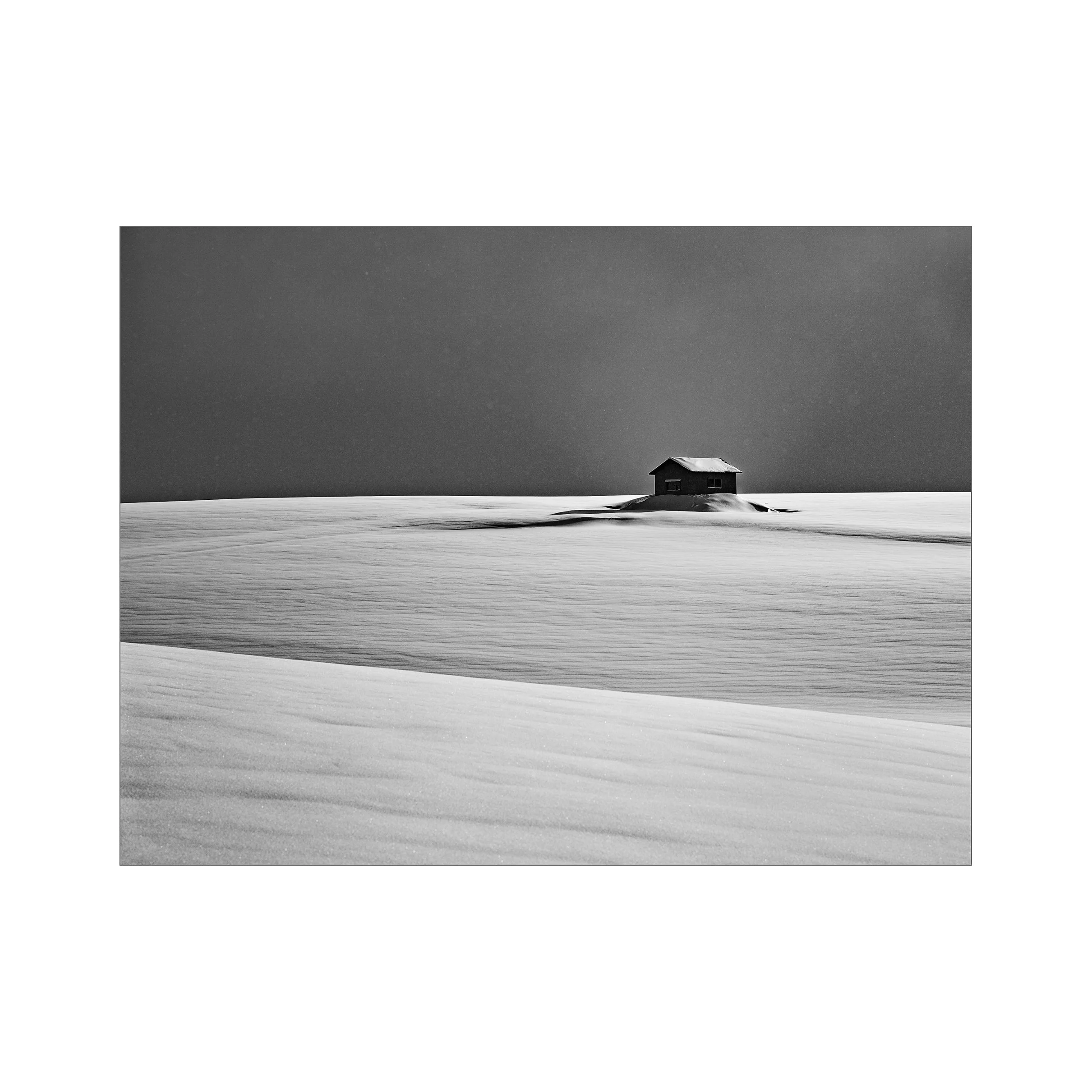 Black and white photo of a house in a snow-covered landscape under a dark sky.