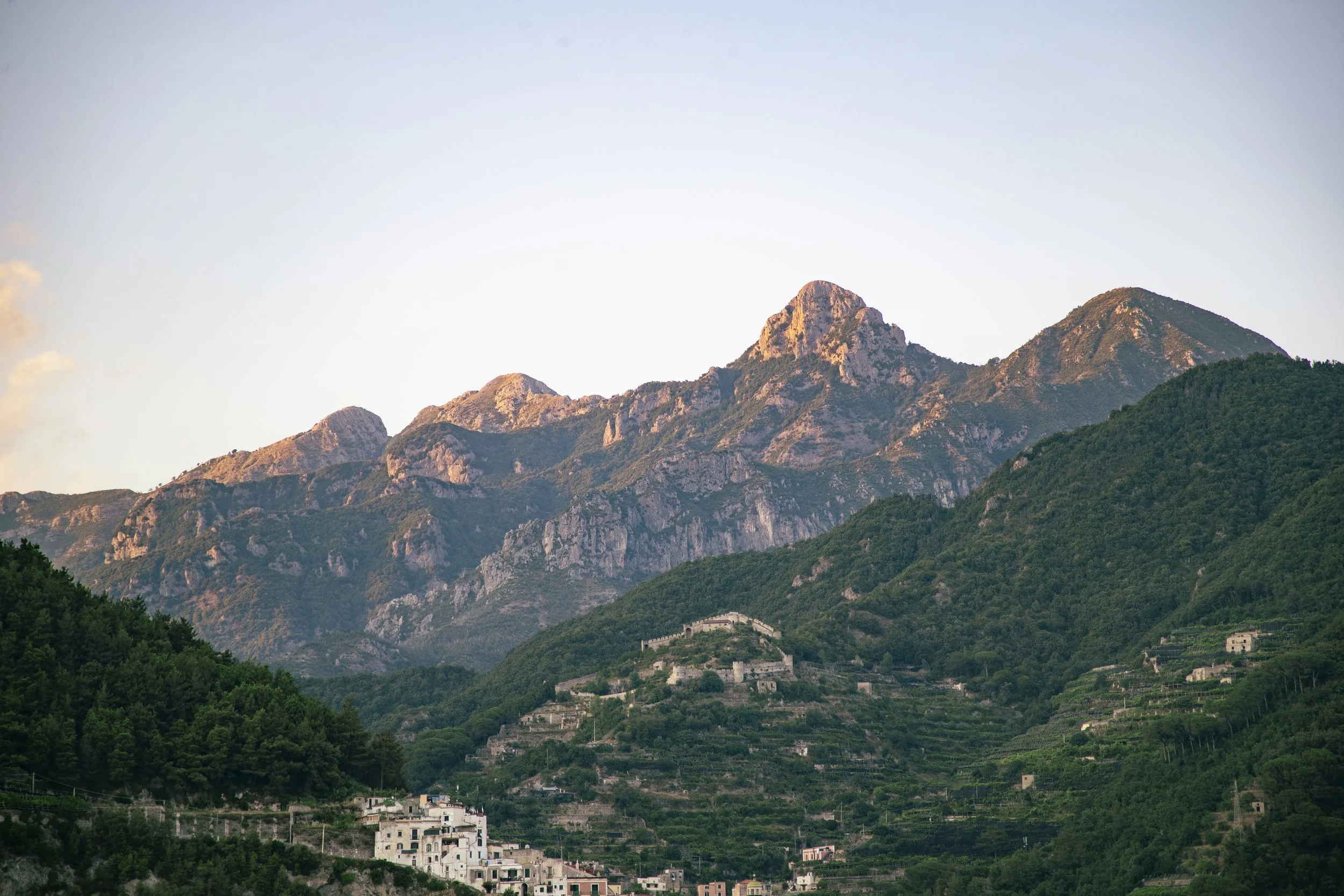 Mountain landscape with green hills and rocky peaks at sunset.