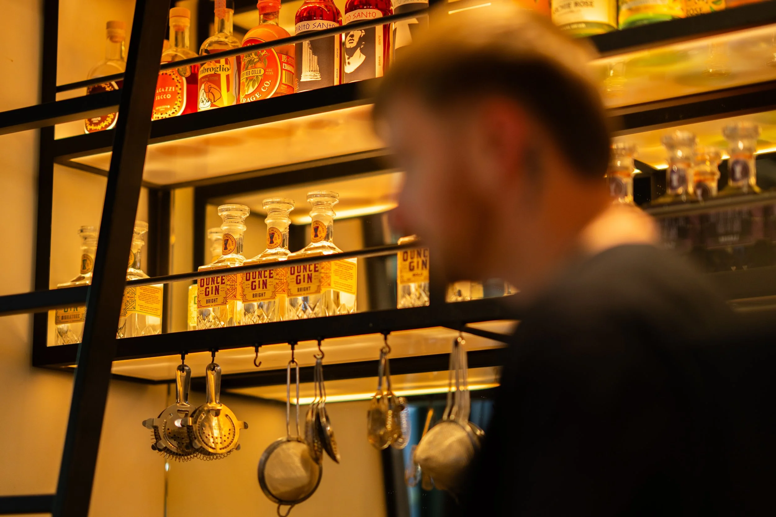 Shelves with bottles of alcohol and hanging utensils in a bar or kitchen.