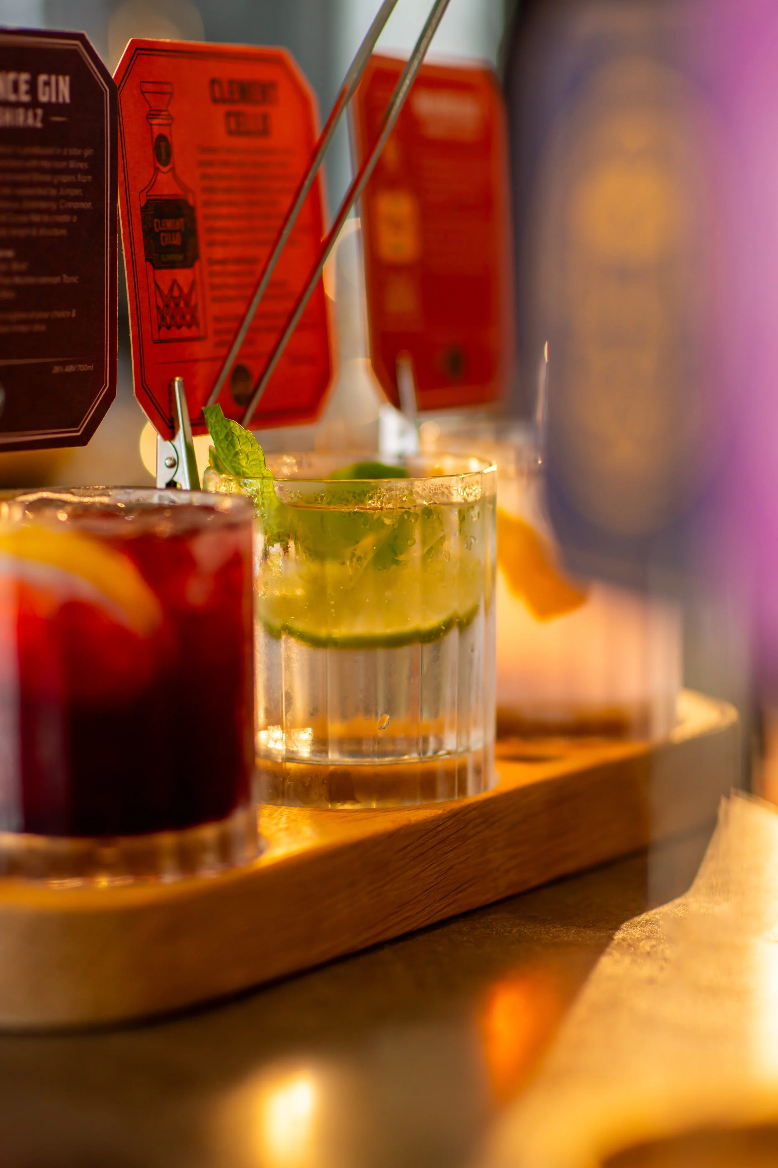 Close-up of cocktails on a wooden tray with bright, colorful lighting.